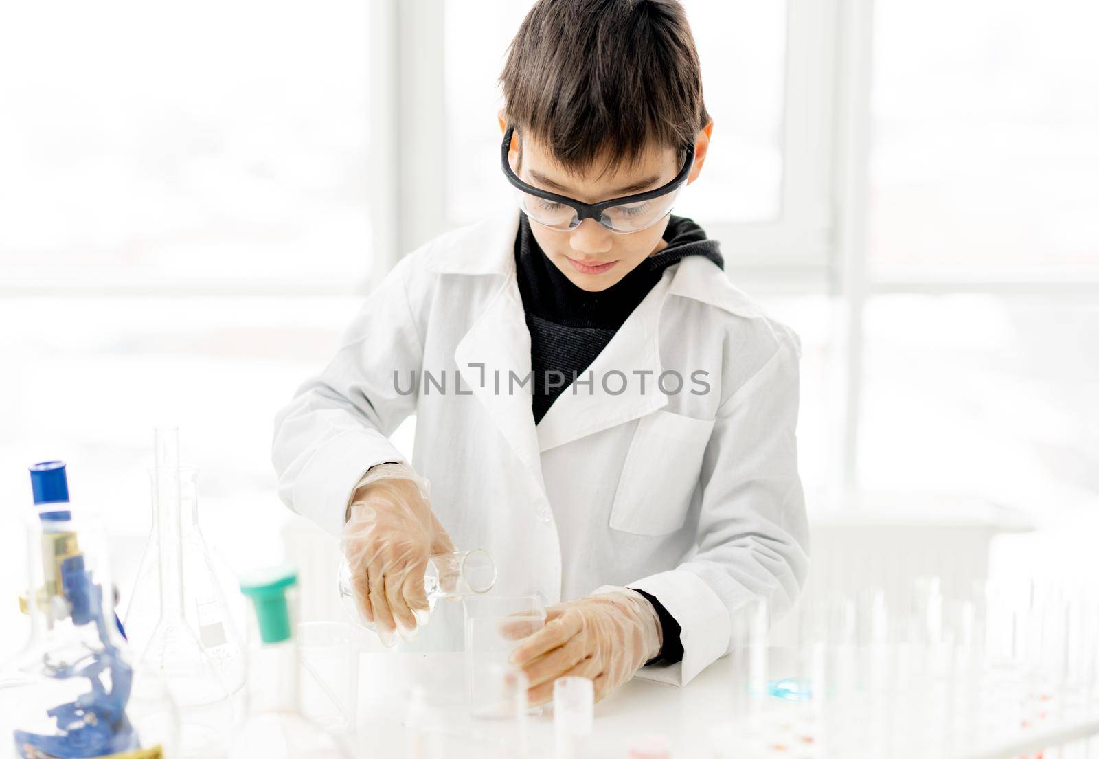 School boy wearing protection glasses doing chemistry experiment in elementary science class. Pupil with equipment tubes in lab