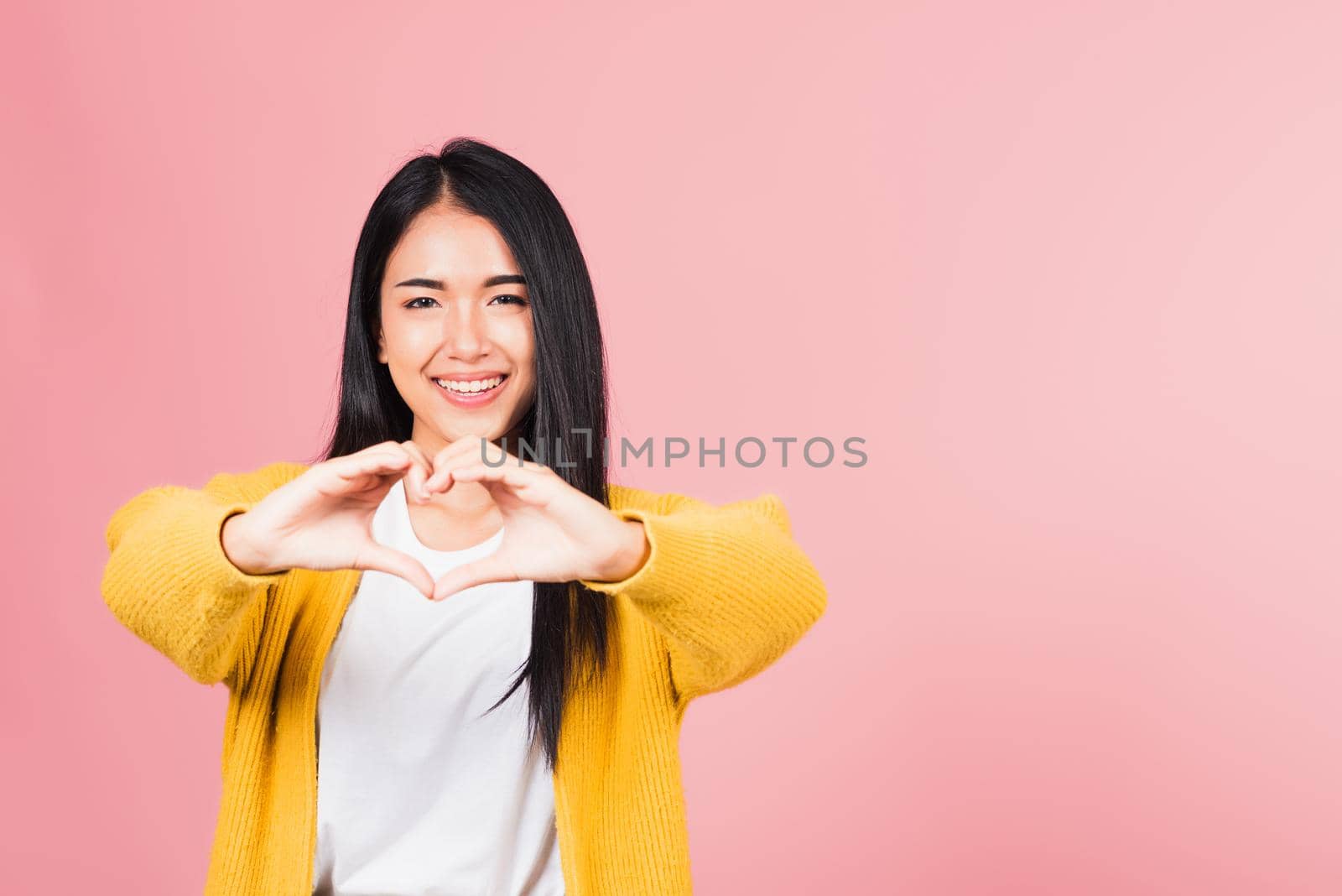 Happy Asian portrait beautiful cute young woman smile make finger heart gesture figure symbol shape sign with two hands sending love to her lover looking camera, studio shot isolated pink background