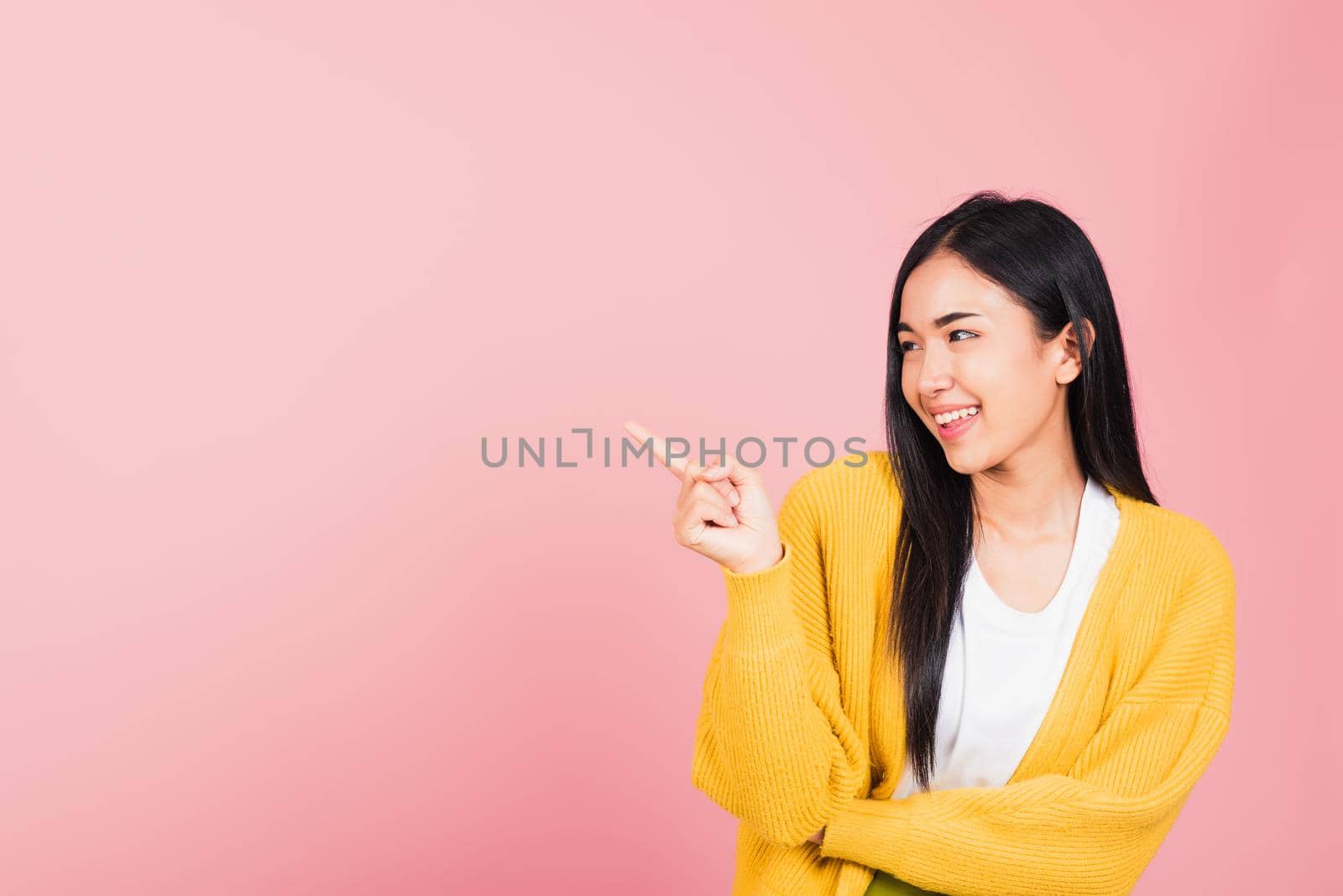 Asian happy portrait beautiful cute young woman standing pointing finger side away presenting product looking to away side, studio shot isolated on pink background with copy space