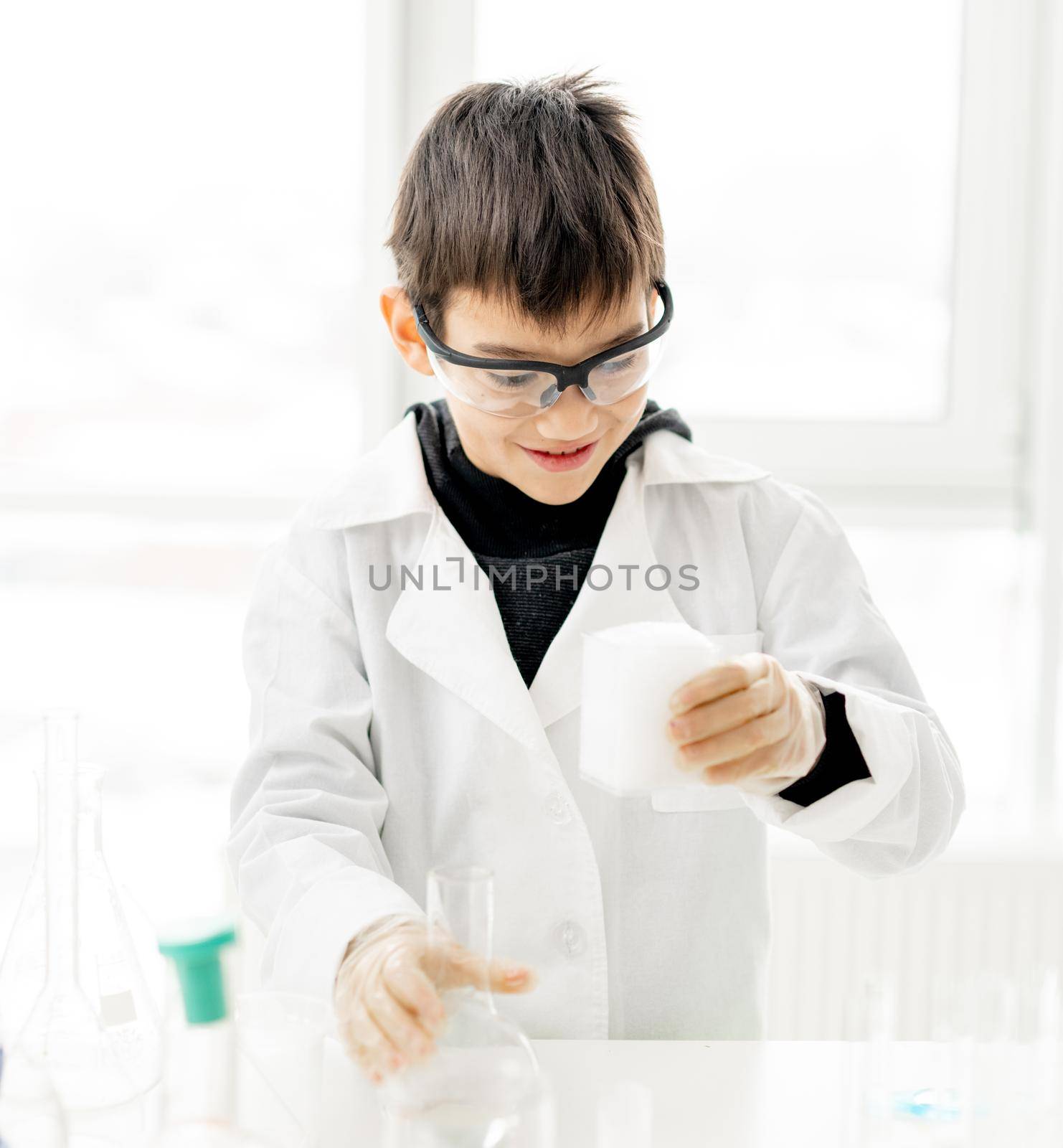 School boy wearing protection glasses doing chemistry experiment in elementary science class. Pupil with equipment tubes in lab during test