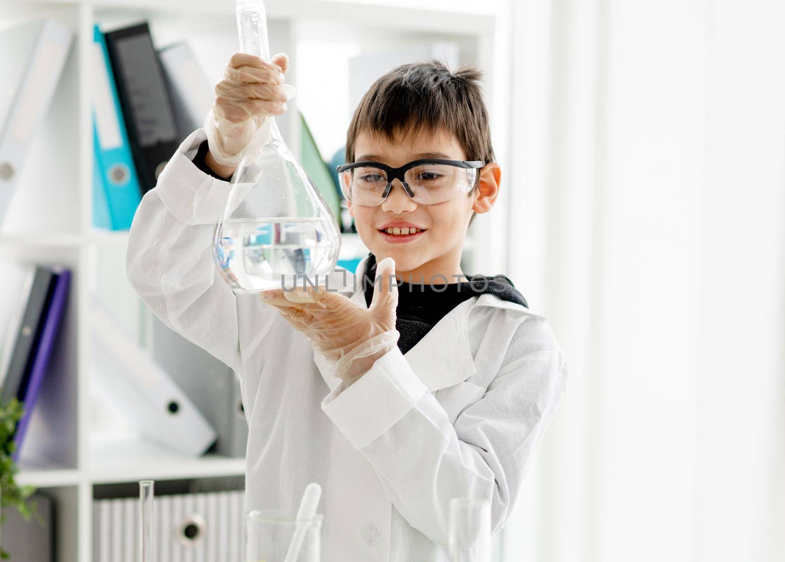 School boy wearing protection glasses doing chemistry experiment in elementary science class. Pupil with equipment tubes in lab during test