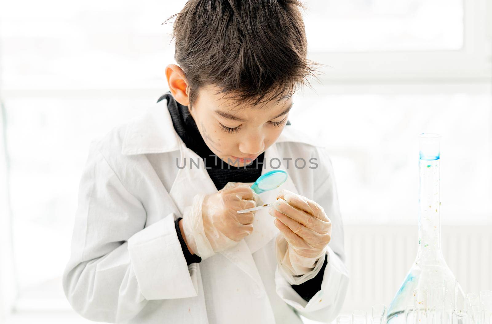 School boy with zoom lens during chemistry experiment in elementary science class. Clever pupil kid in lab