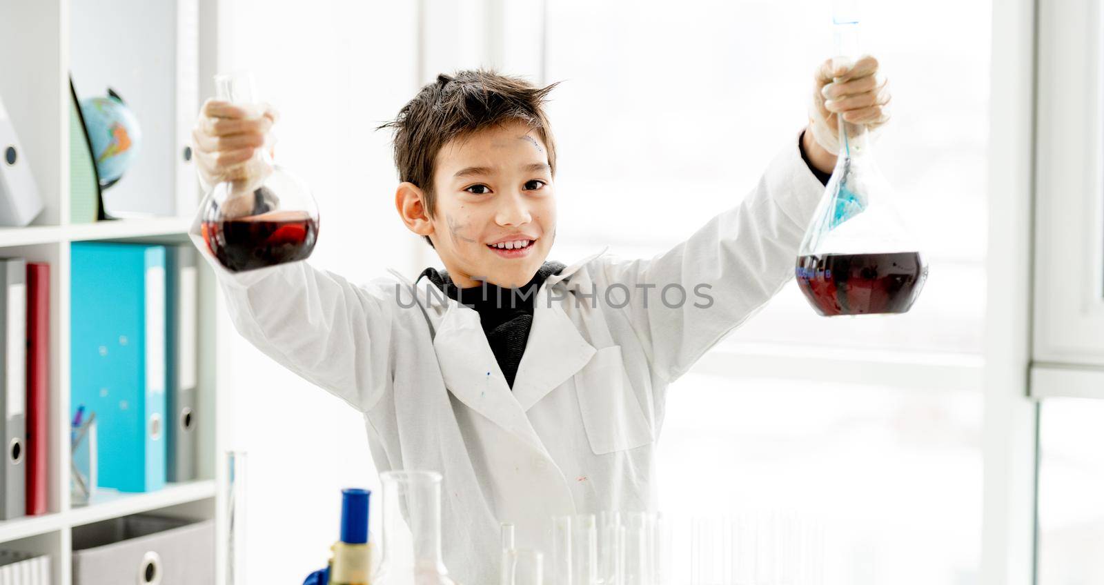 School boy holding two bottles with chemical liquids during chemistry experiment in elementary science class. Clever pupil kid in lab