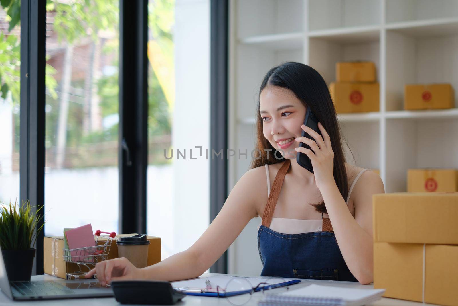 Business owner confirm address to send to customer orders talking by cell phone before pack products. Successful SME entrepreneur concept. by itchaznong