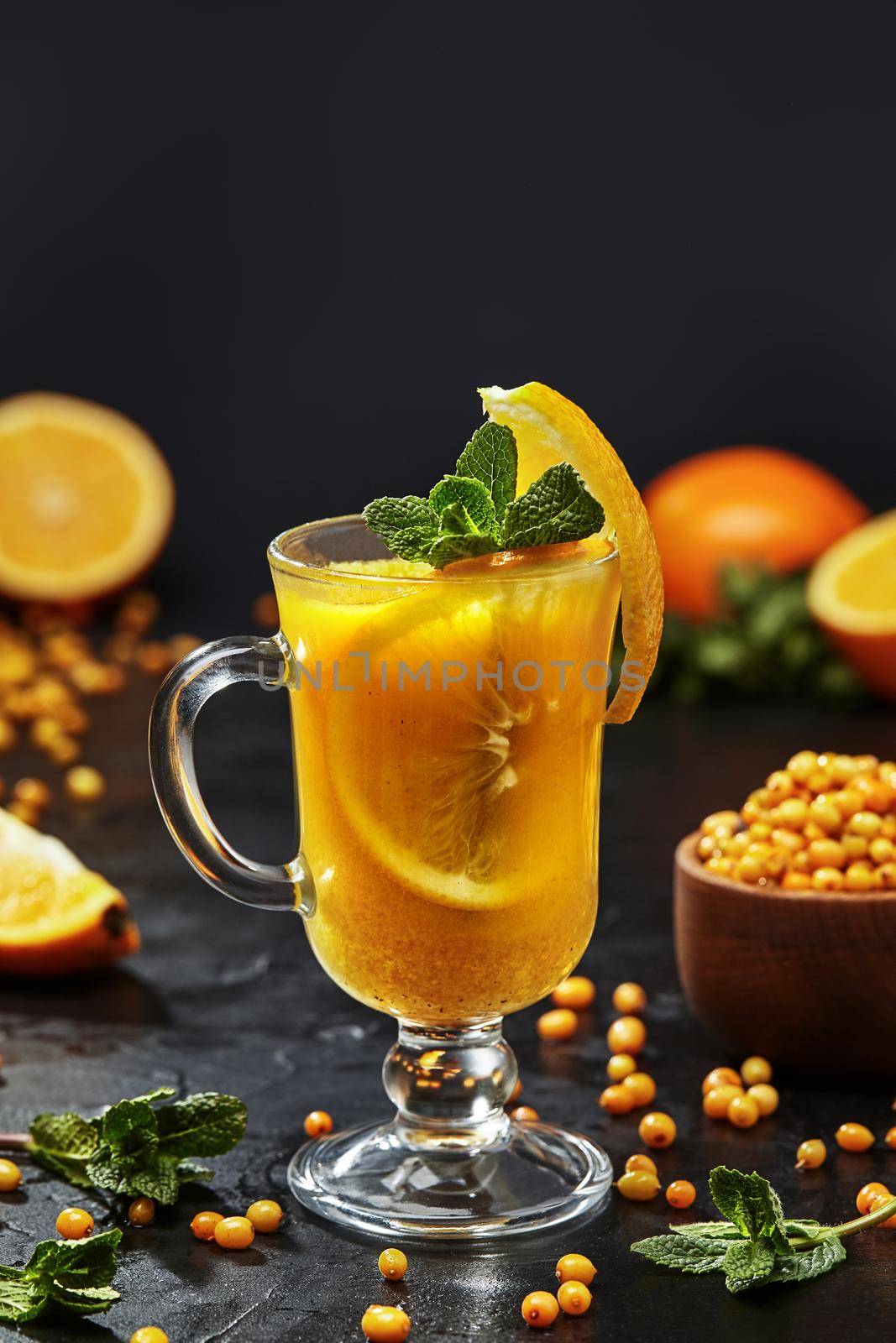 Vitamin aromatic fruit and berry tea from ripe sea buckthorn and orange with cinnamon and fresh fragrant mint leaves in glass on black background. Healthy and immune-boosting drinks concept