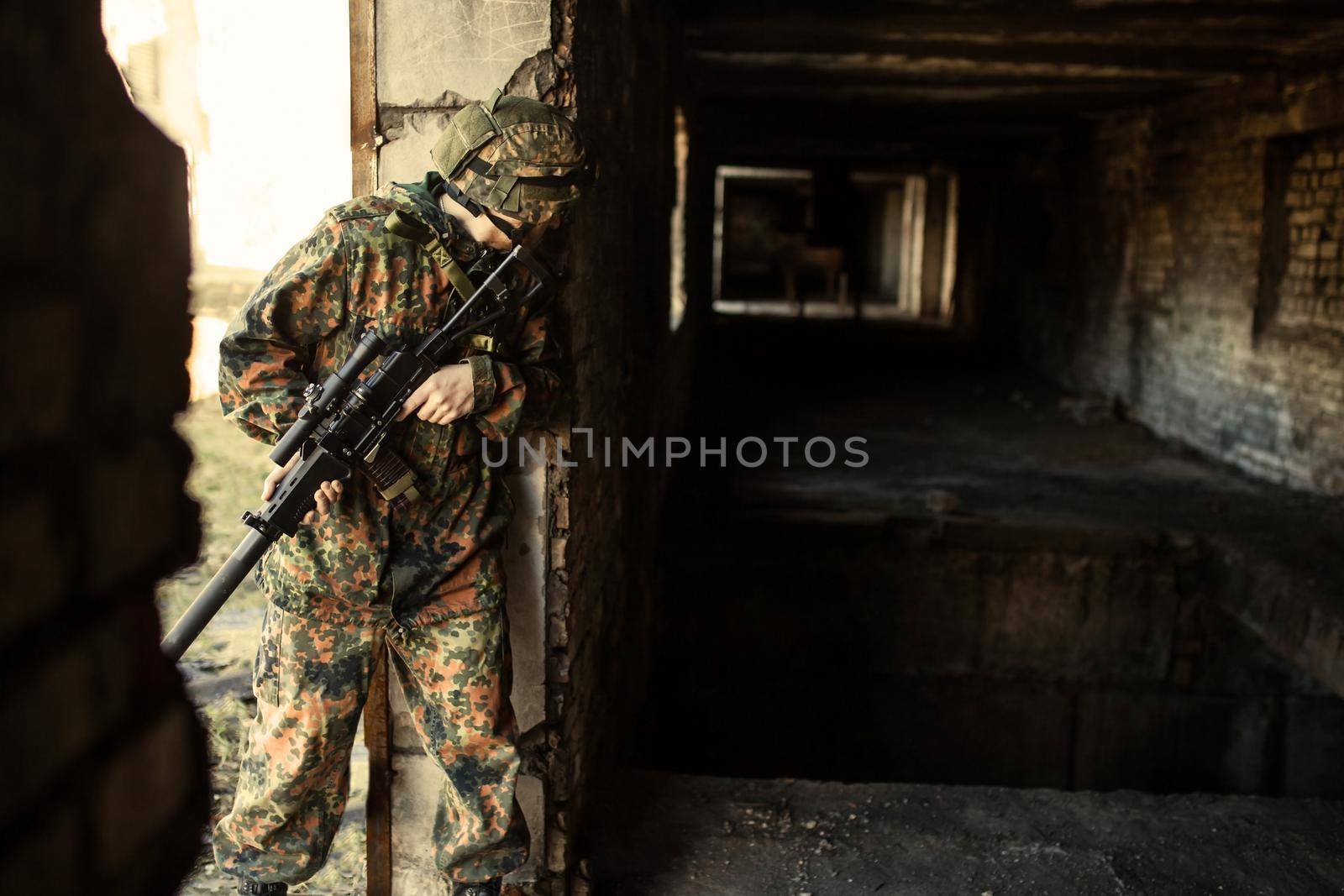 young soldiers with guns, A soldier in equipment and with arms inspects a ruined house outside the city.