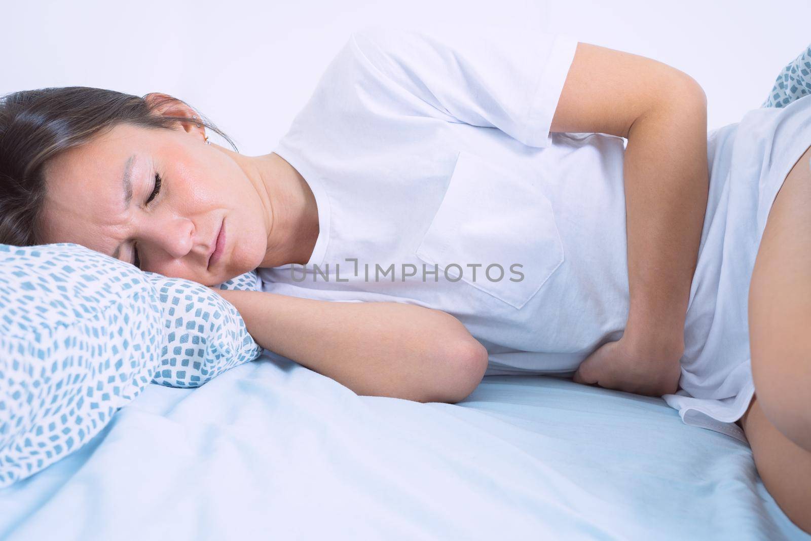 Young woman lying in the bed and suffering from gynecological problems, menstruation pain, stomach ache or abdominal pain. Menstruation period or PMS by DariaKulkova