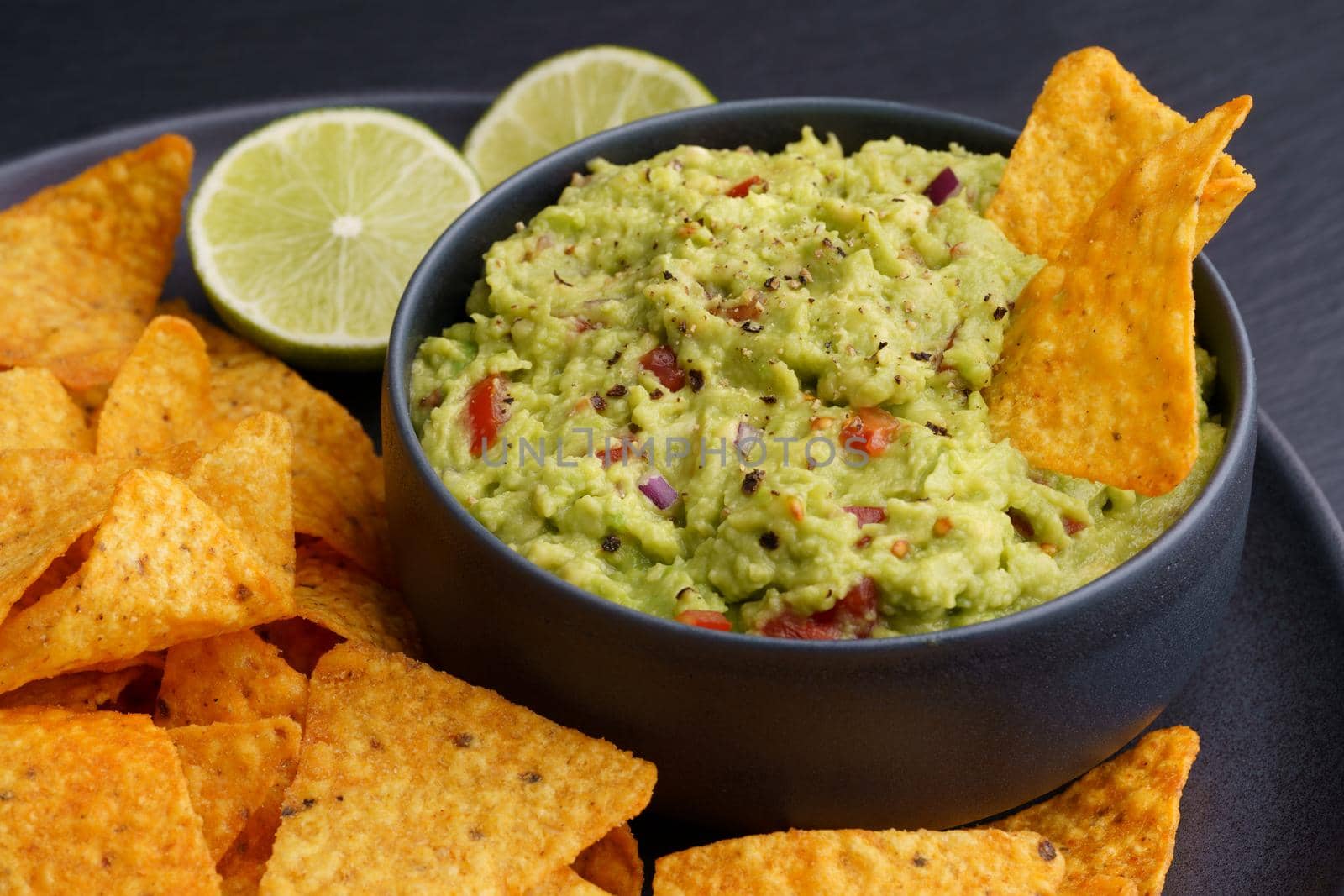 Guacamole dip with tortilla chips or nachos in black plate on a black background. High quality photo
