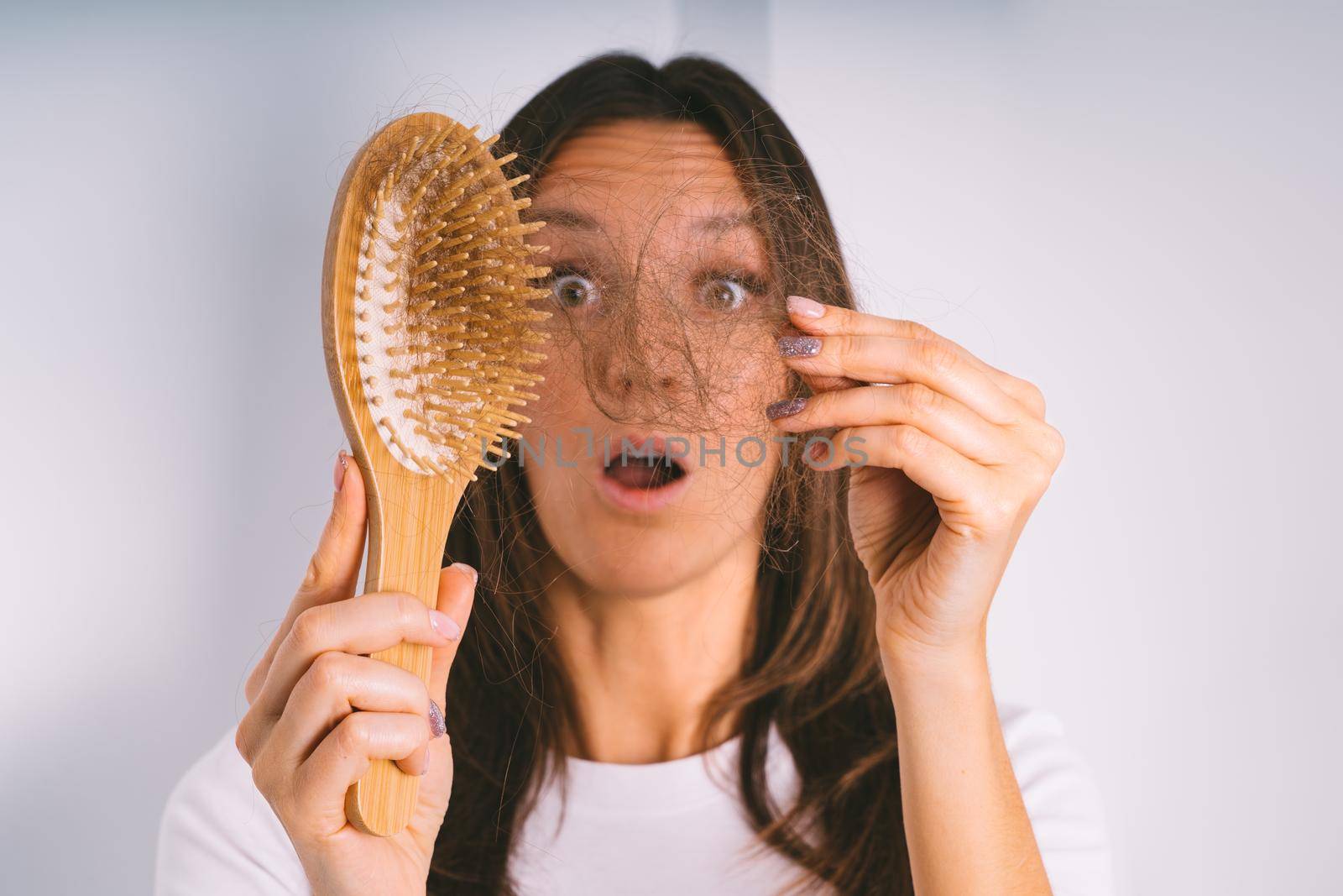 Young woman shocked because of hair loss problem. Woman holding hair brush and showing damaged hair. Bad hair falling out by DariaKulkova