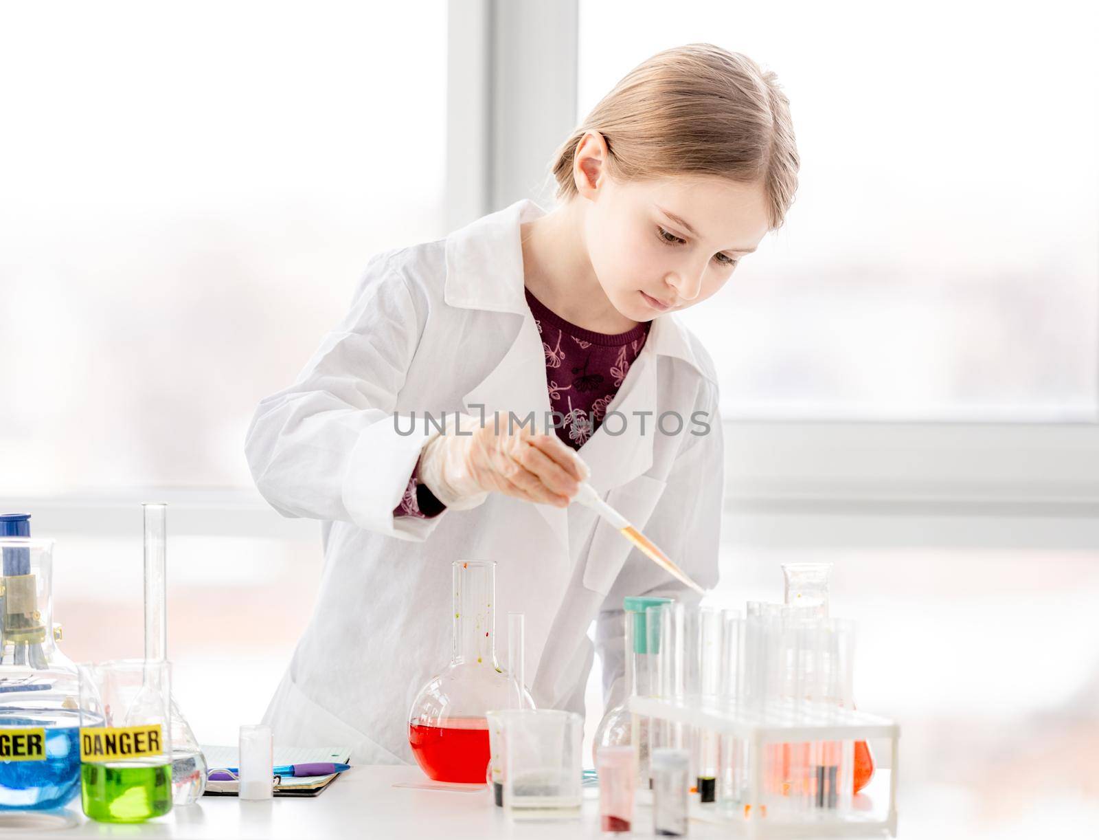 Smart girl during scientific chemistry experiment wearing protection glasses, holding tubes and measuring ingridients. Schoolgirl with chemical equipment on school lesson