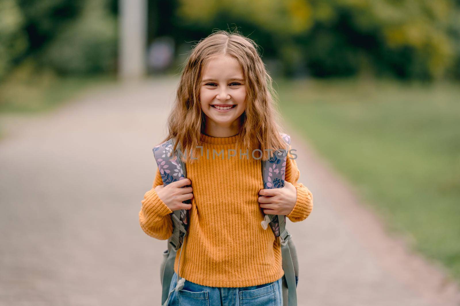 Beautiful girl child with back pack after school smiling and looking at camera. Portrait of preteen female kid outdoors at autumn
