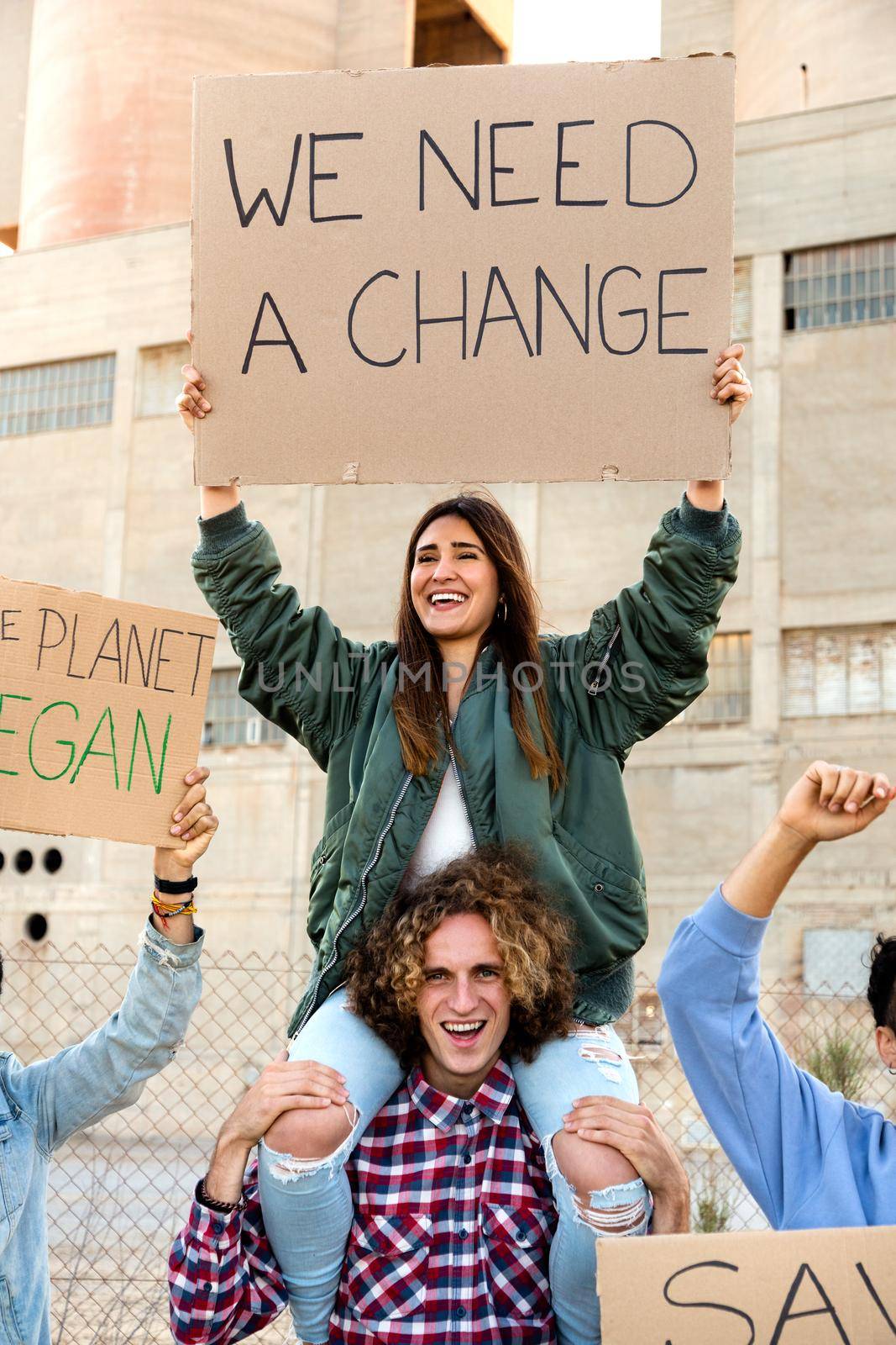 Happy young hispanic woman sitting on mans shoulder protesting against climate change in demonstration. Vertical image. Activist concept.