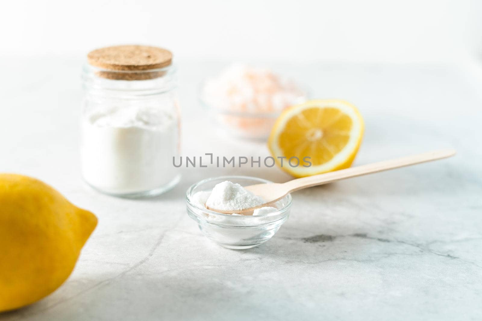 Eco friendly natural cleaners, jar with baking soda, lemon, pink salt and wooden spoon on marble table background. Organic ingredients for homemade cleaning. Zero waste concept.