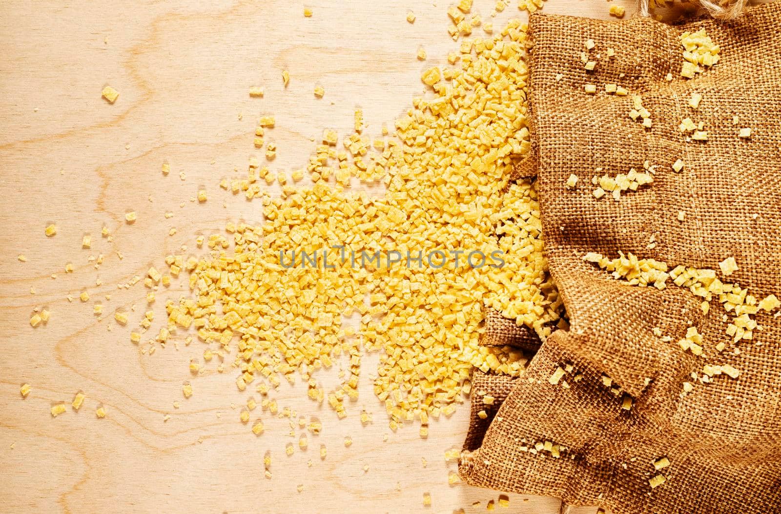  Small flat squares  egg pasta called grattini on brown bag on wooden background,yellow  pasta with rough surface 