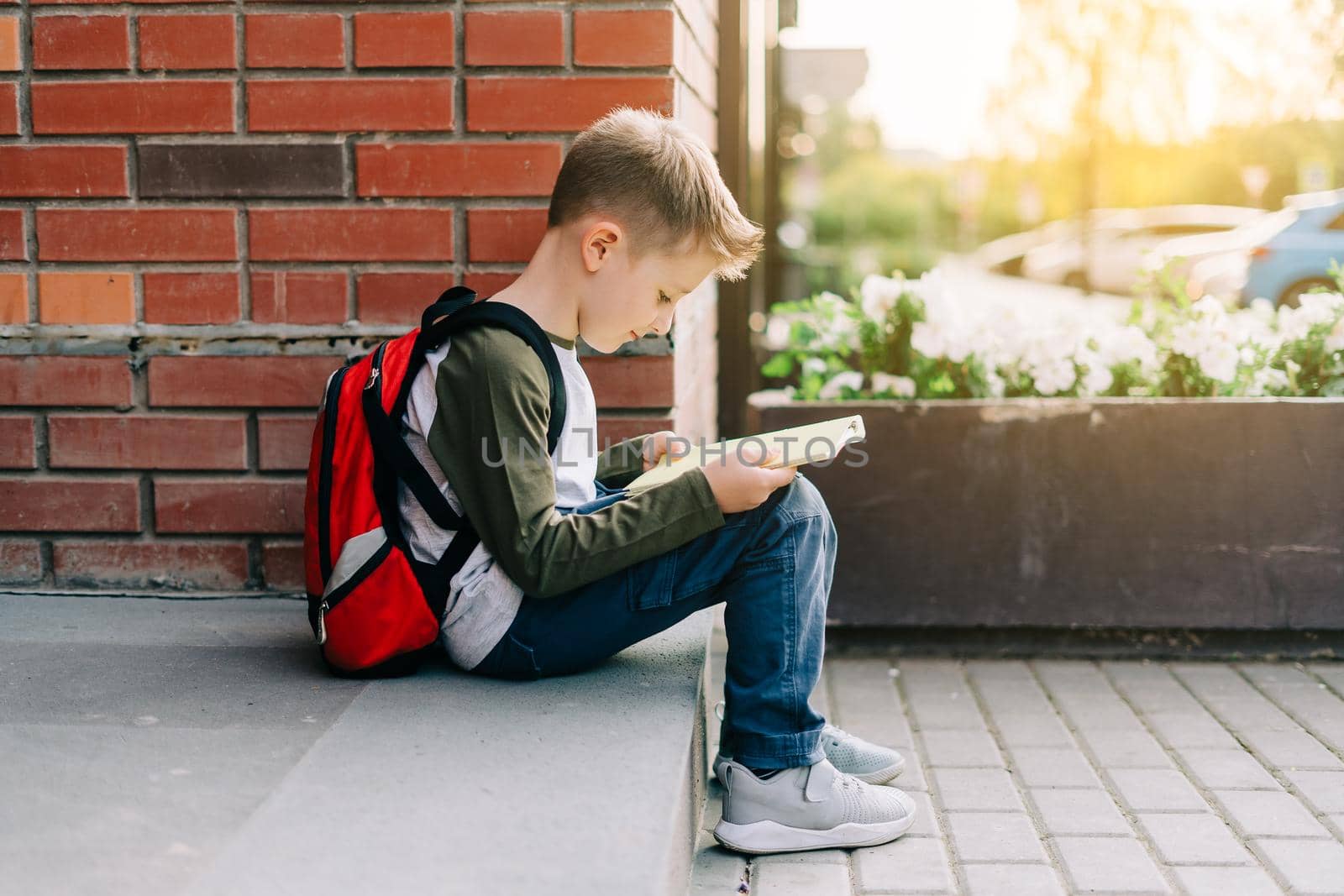 Back to school. Cute child with backpack, holding notepad and training books. School boy pupil with bag. Elementary school student going to classes. Kid sitting on stairs outdoors at brick wall.