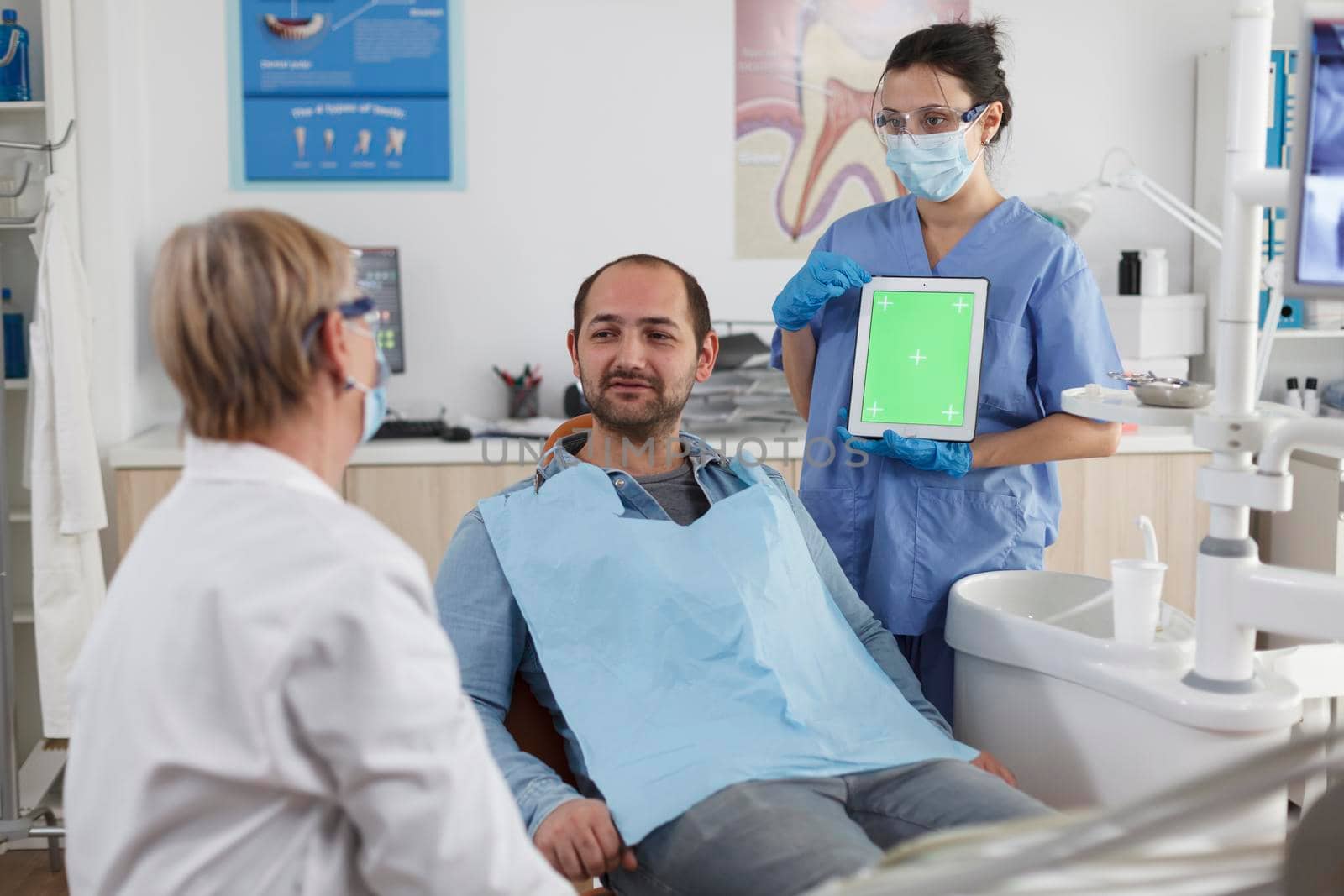 Stomatology medical team discussing dentistry treatment with patient during stomatological consultation in dental office. Nurse holding mock up green screen chroma key tablet with isolated display