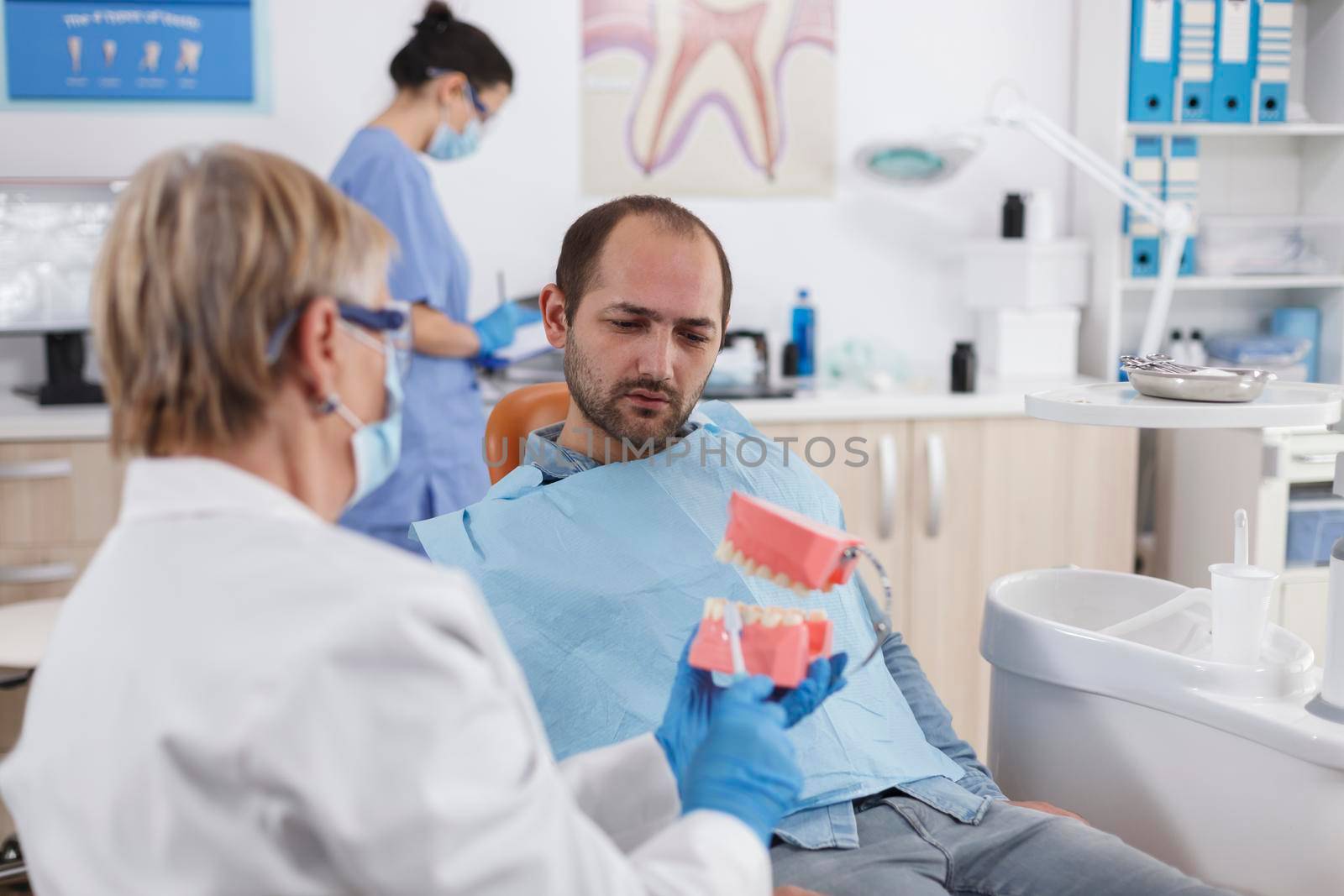 Senior woman doctor showing artificial jaw model to patient by DCStudio