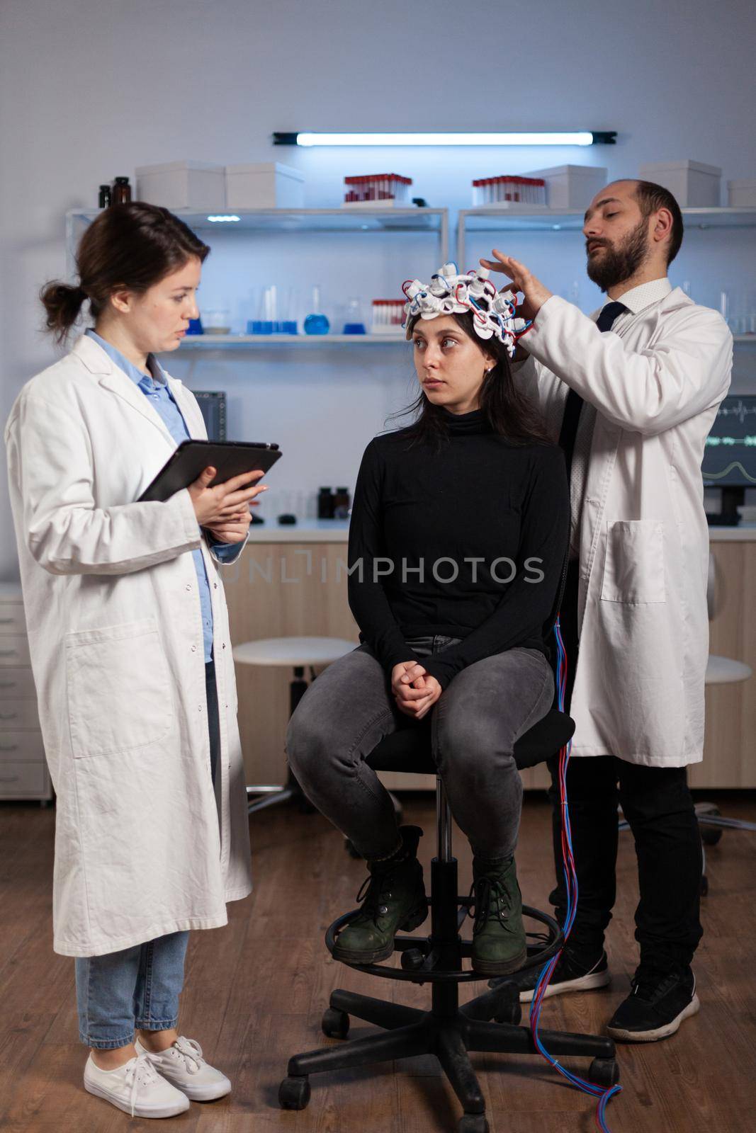Scientist doctor explaining neurology disease symptoms to woman patient while neurologist researcher adjusting eeg headset during neuroscience experiment in lab. Specialist analyzing brain activity