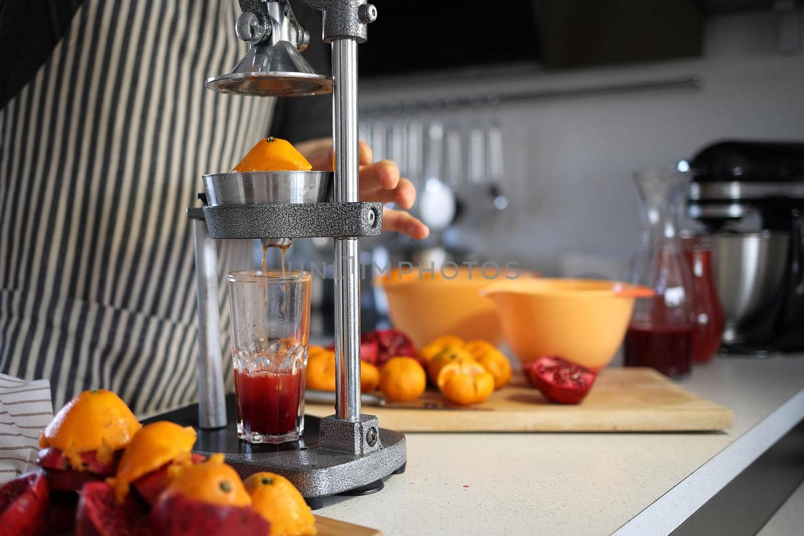 man squeezes juice from pomegranates and tangerines using a hand press at home by Proxima13