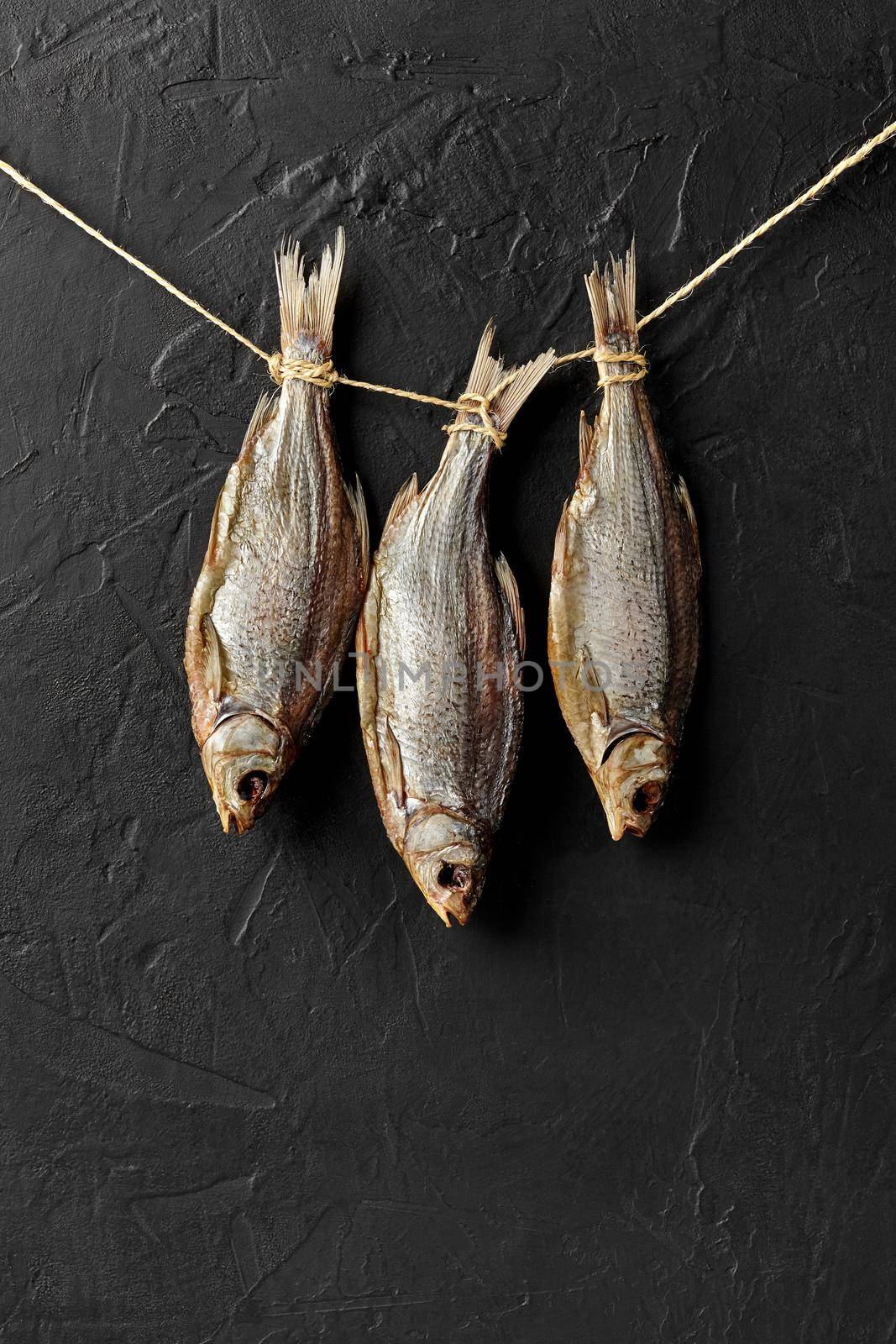 Three salt-dried roaches hanging on rope on black wall background. Traditional beer snack