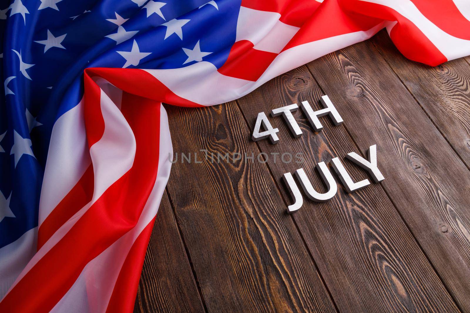 the words 4th july and crumpled usa flag on flat textured wooden surface background.
