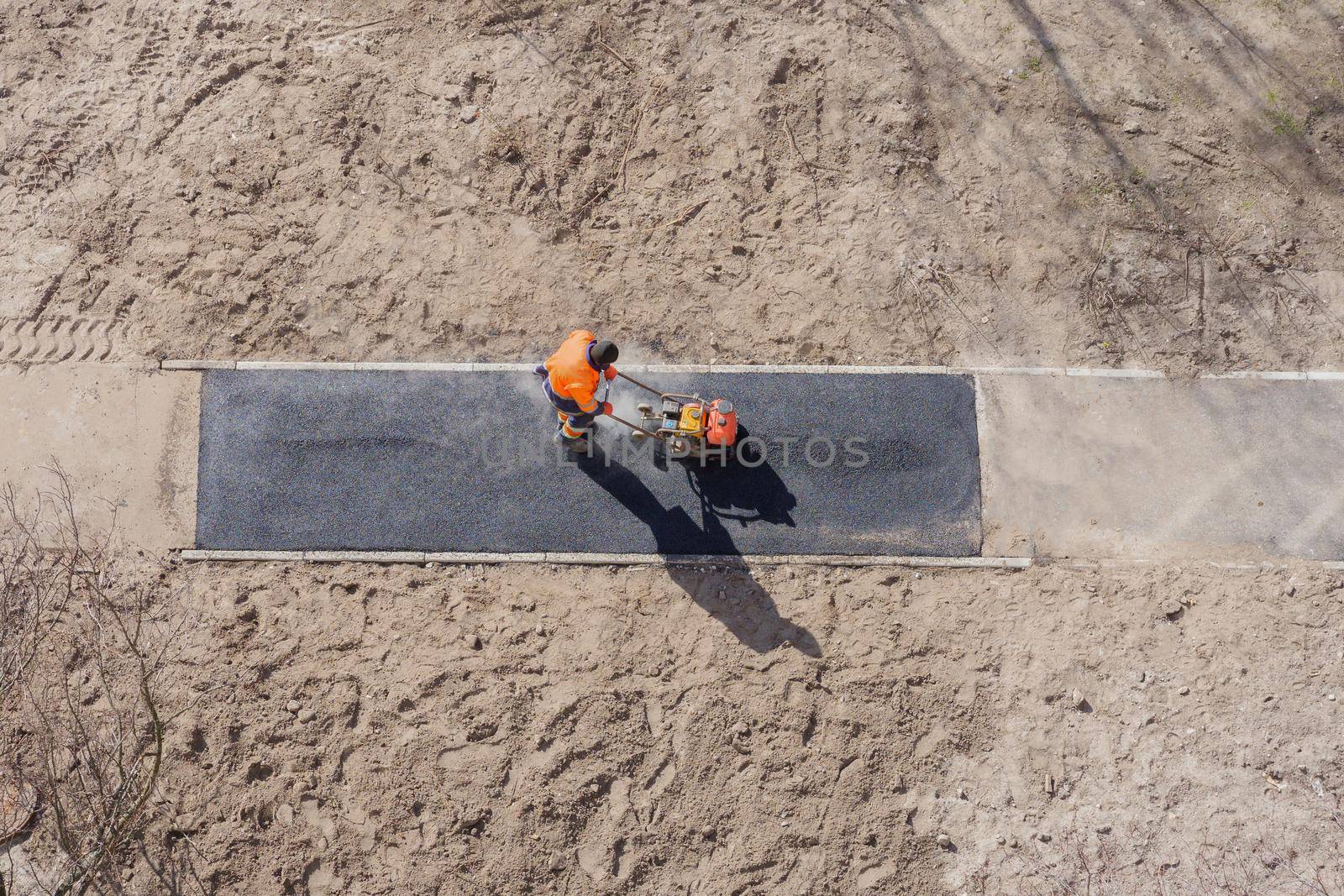 New asphalt construction worker laying road surface on walkway work tarmac. Sidewalk construction road ground work asphalt. Groundwork asphalt paving road worker with vibratory plate compactor rammer by synel