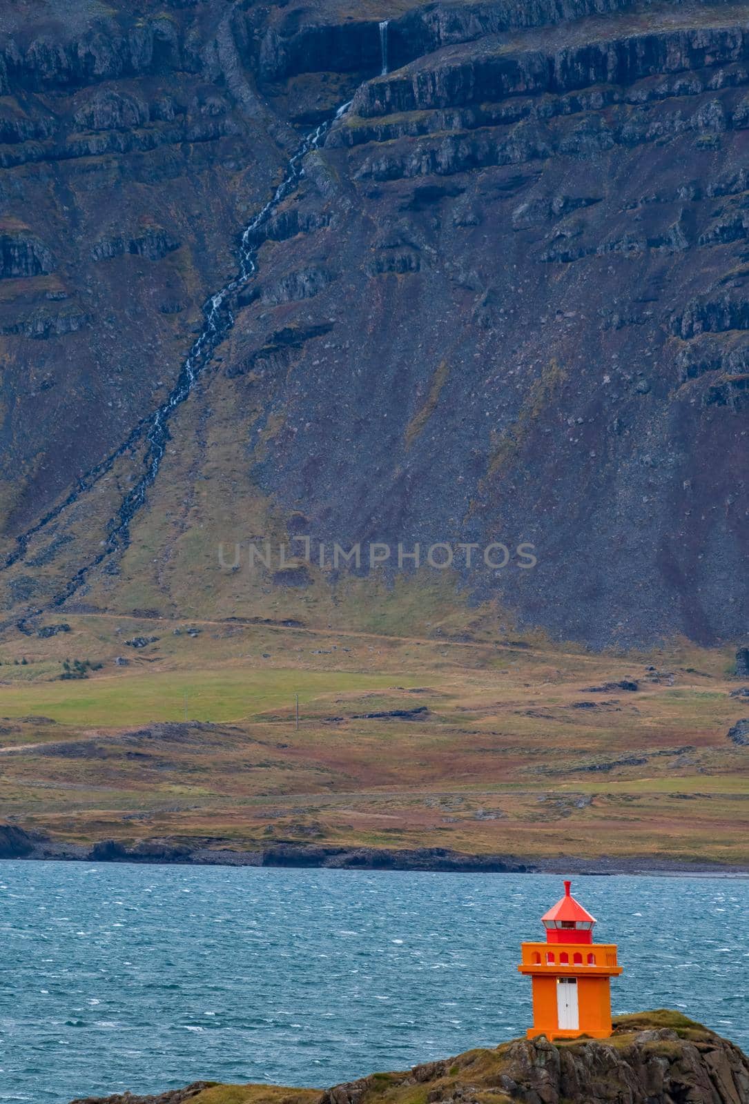 Orange lighthouse near the fjord shore in Iceland, vertical composition
