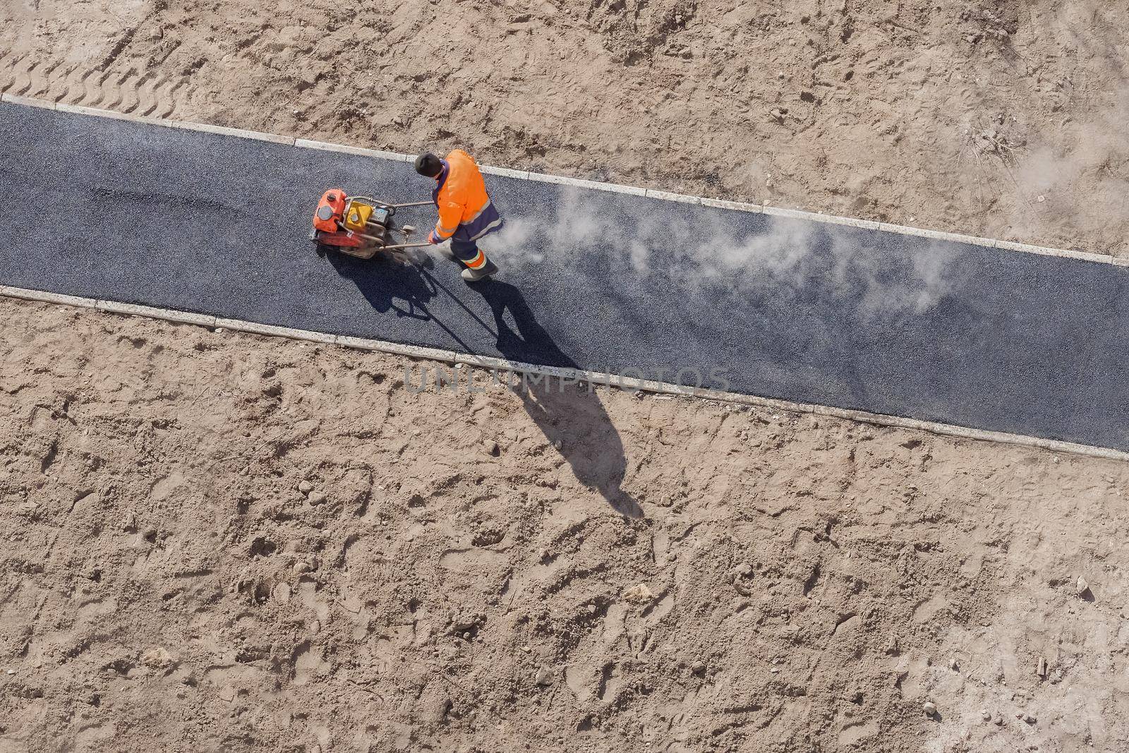 Hot asphalt paving road construction site work man vibratory plate compactor rammer. New road construction worker laying asphalt surface on walkway work. Sidewalk construction asphalt work road tarmac by synel