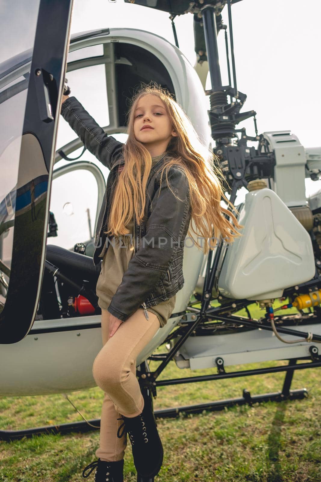 Confident preteen girl with long light brown hair standing on footboard of open helicopter at field of flying club