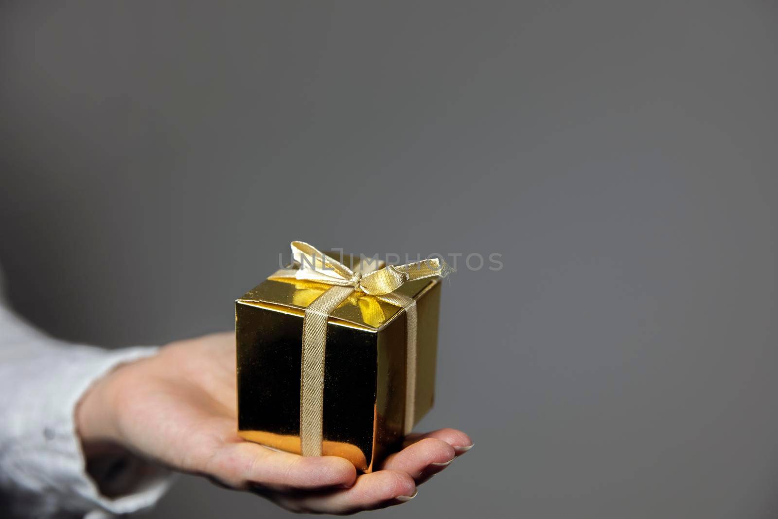 Hands holding gold gift box isolated on gray background. giving present, Birthday,Christmas,Mothersday other Holiday with copy space space for text