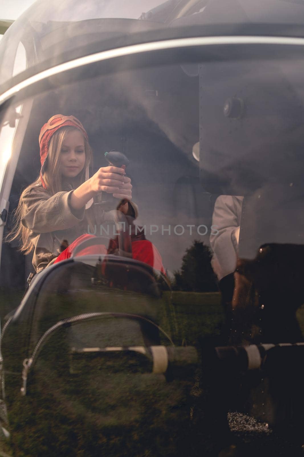 View through glass of helicopter cockpit of focused preteen girl sitting on co-pilot seat imitating aircraft control. Childhood dream of becoming aviator