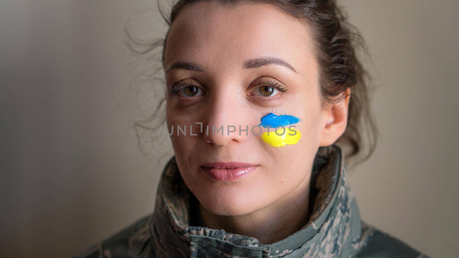 Indoor portrait of young girl with blue and yellow ukrainian flag on her cheek wearing military uniform, mandatory conscription in Ukraine, equality concepts by balinska_lv