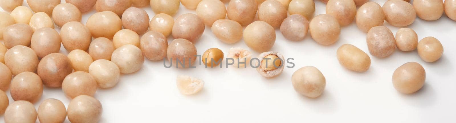 Heap of sweet roasted peanuts in sugar glaze scattered on white surface. Closeup of whole and broken dragees. Popular cracker nuts. Natural food background. Horizontal image with copyspace