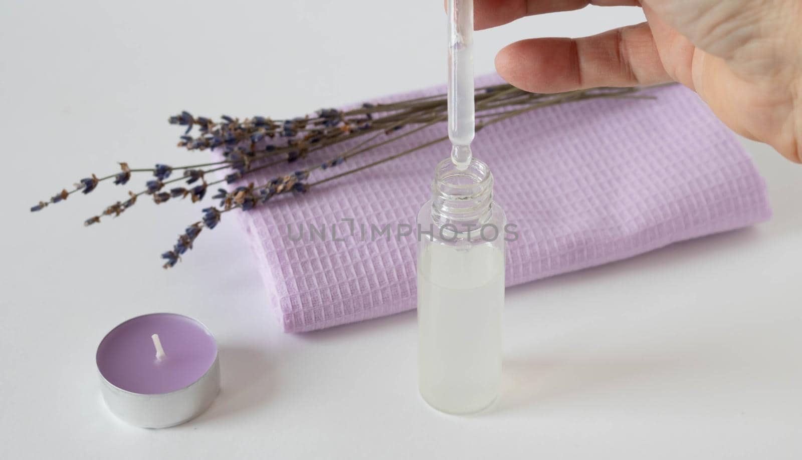 Sprigs of dried lavender and an aromatic lavender candle with a lilac towel, a bottle with an eyedropper on a white background. The concept of harmony. The concept of aromatherapy.