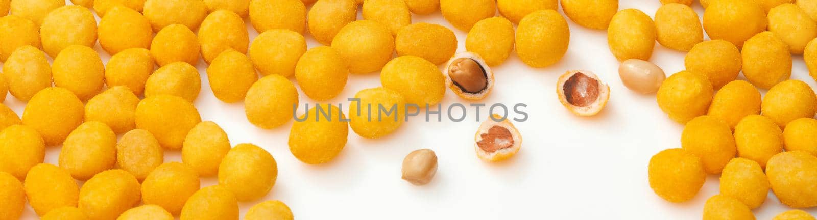 Appetizing roasted peanuts in yellow salty crunchy shell with bacon flavor scattered on white surface. Closeup of whole and broken glazed balls. Popular snacks concept. Natural food background