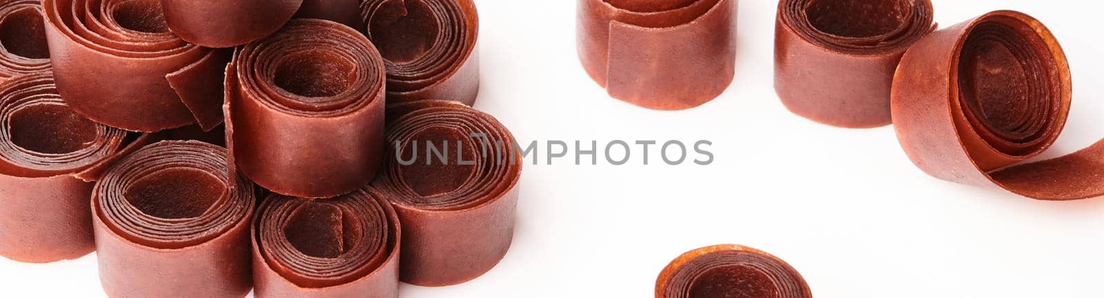 Traditional Georgian tklapi rolls, pureed sun-dried fruit leather on white background. Concept of popular organic sweets and authentic cuisine. Horizontal image with copy space