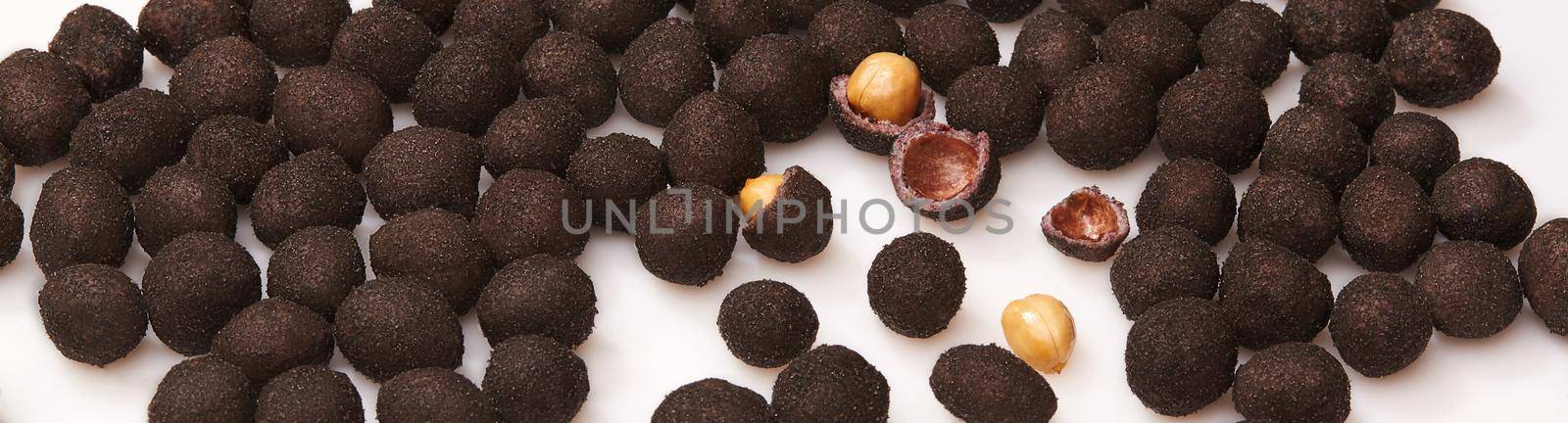 Delicious roasted peanuts in sweet crunchy shell from cocoa and powdered sugar scattered on white surface. Closeup of whole and broken brown glazed dragees. Popular snacks. Natural food background