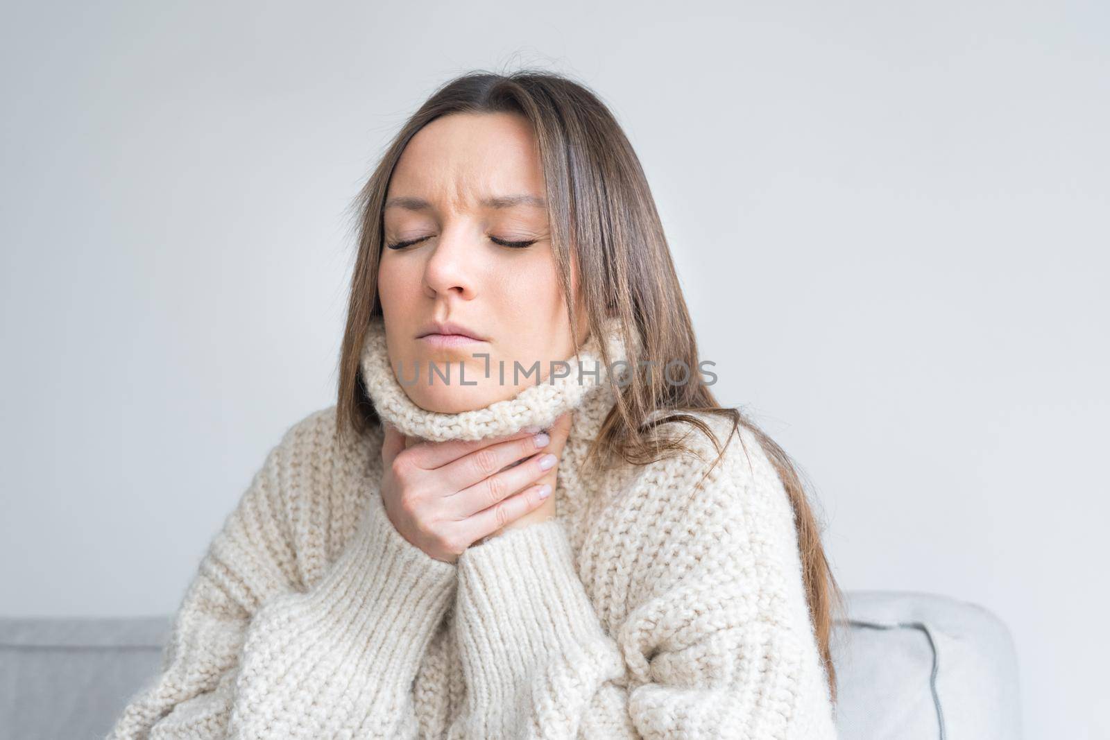 Young woman in cozy sweater touching painful neck. Sore throat, inflamed throat. Coronavirus symptom. High quality photo
