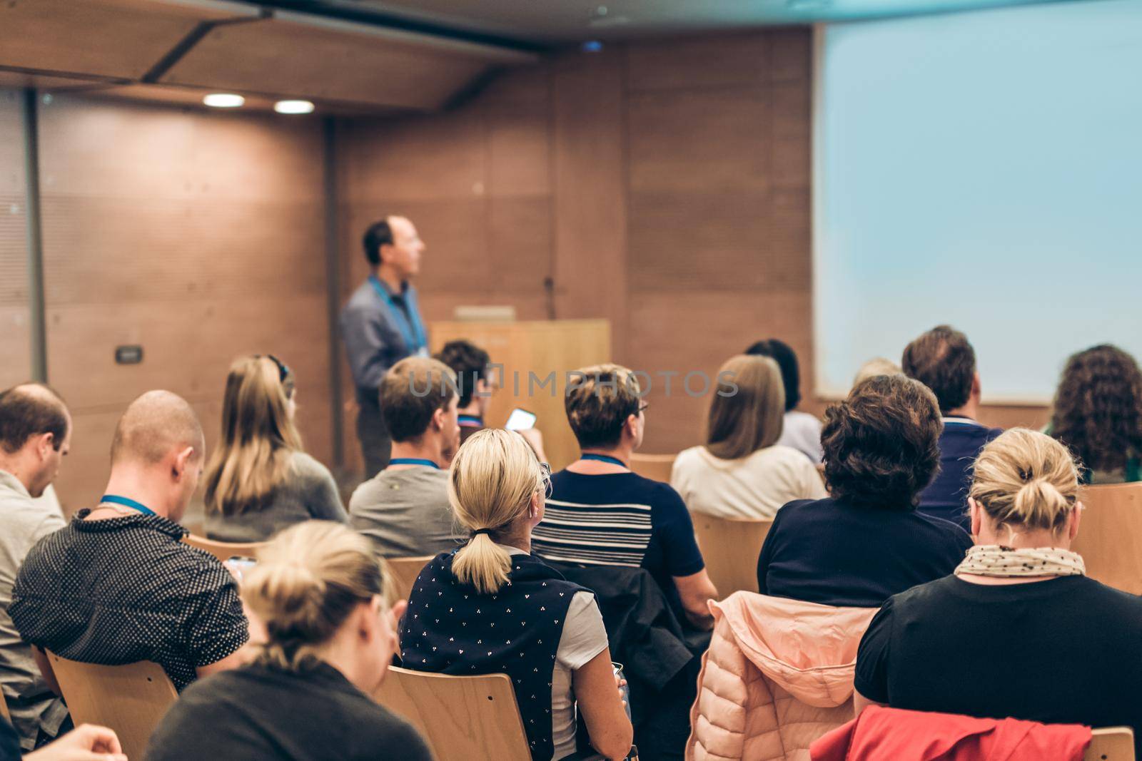 Speaker Giving a Talk at Business Meeting. Audience in the conference hall. Business and Entrepreneurship. Focus on unrecognizable people from rear.