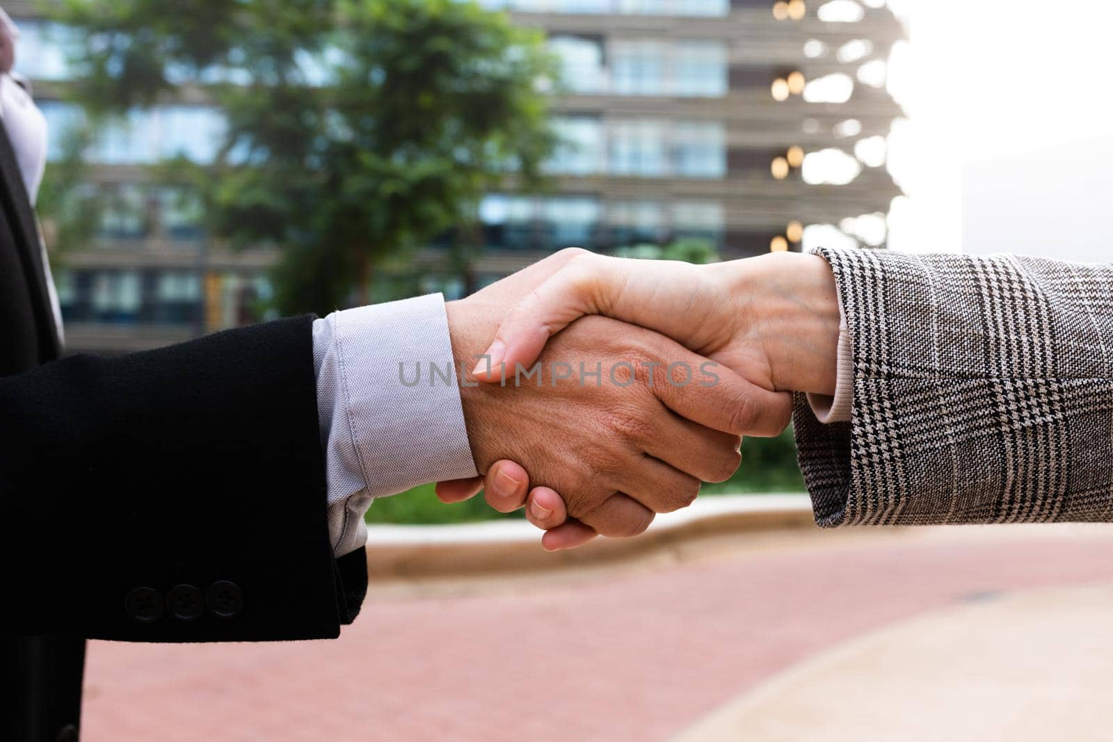 Business man and woman shake hands outside office buildings. Handshake. by Hoverstock