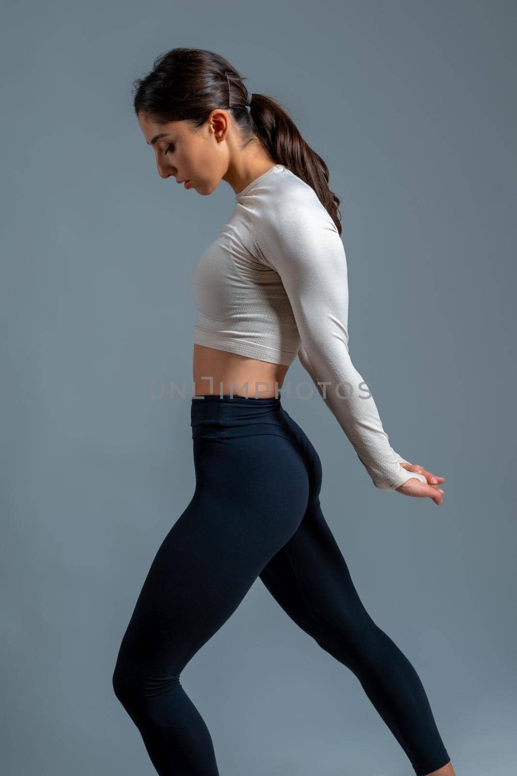 Side view of confident young sportswoman warming up before intense workout, doing stretching exercises. Crop shot in studio on grey background