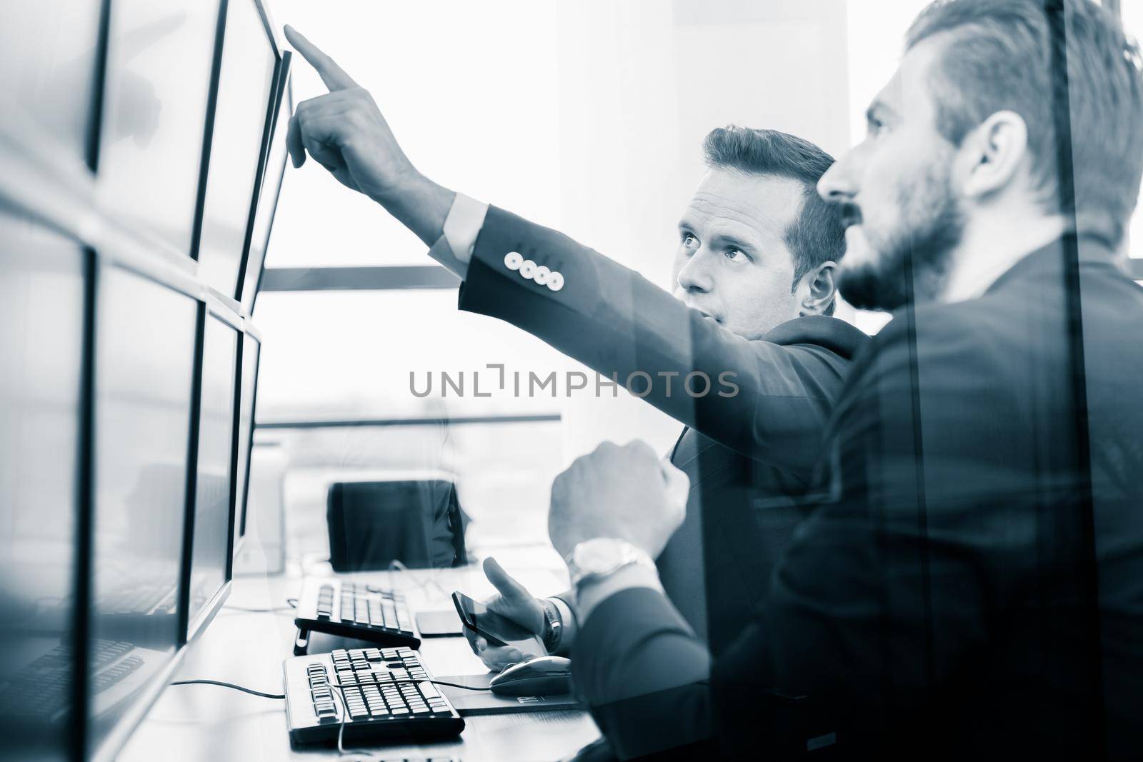 Businessmen trading stocks. Stock traders looking at graphs, indexes and numbers on multiple computer screens. Colleagues in discussion in traders office.