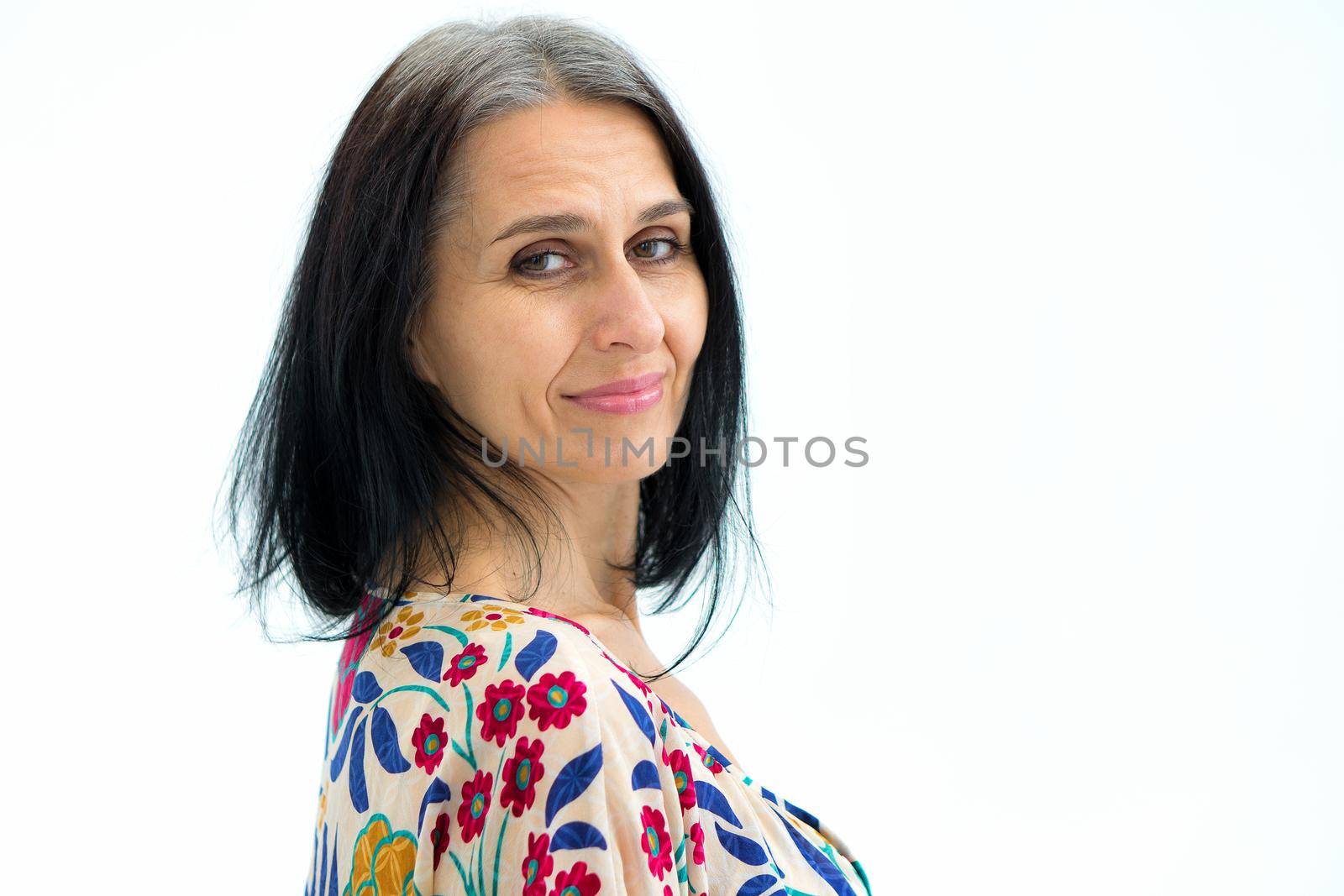 Close-up portrait of middle aged woman starting getting grey-haired wearing dress with flowers on white background, middle age sexy lady, cosmetology concept by balinska_lv