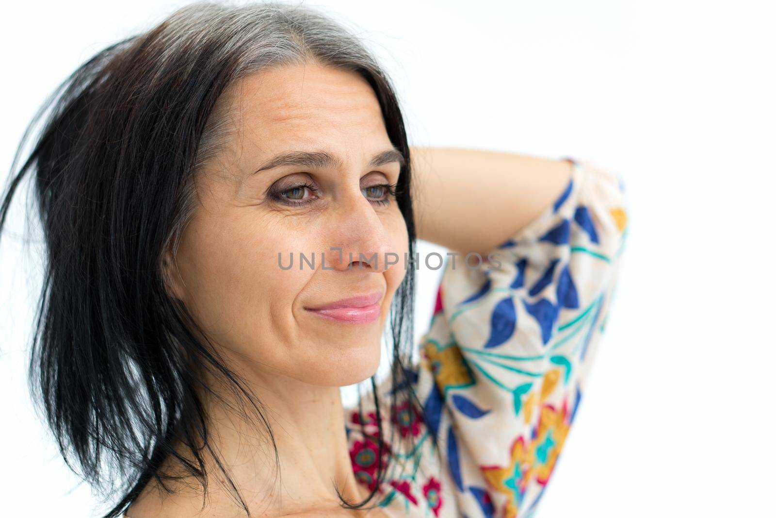 Close-up portrait of middle aged woman starting getting grey-haired wearing dress with flowers on white background, middle age sexy lady, cosmetology concept.