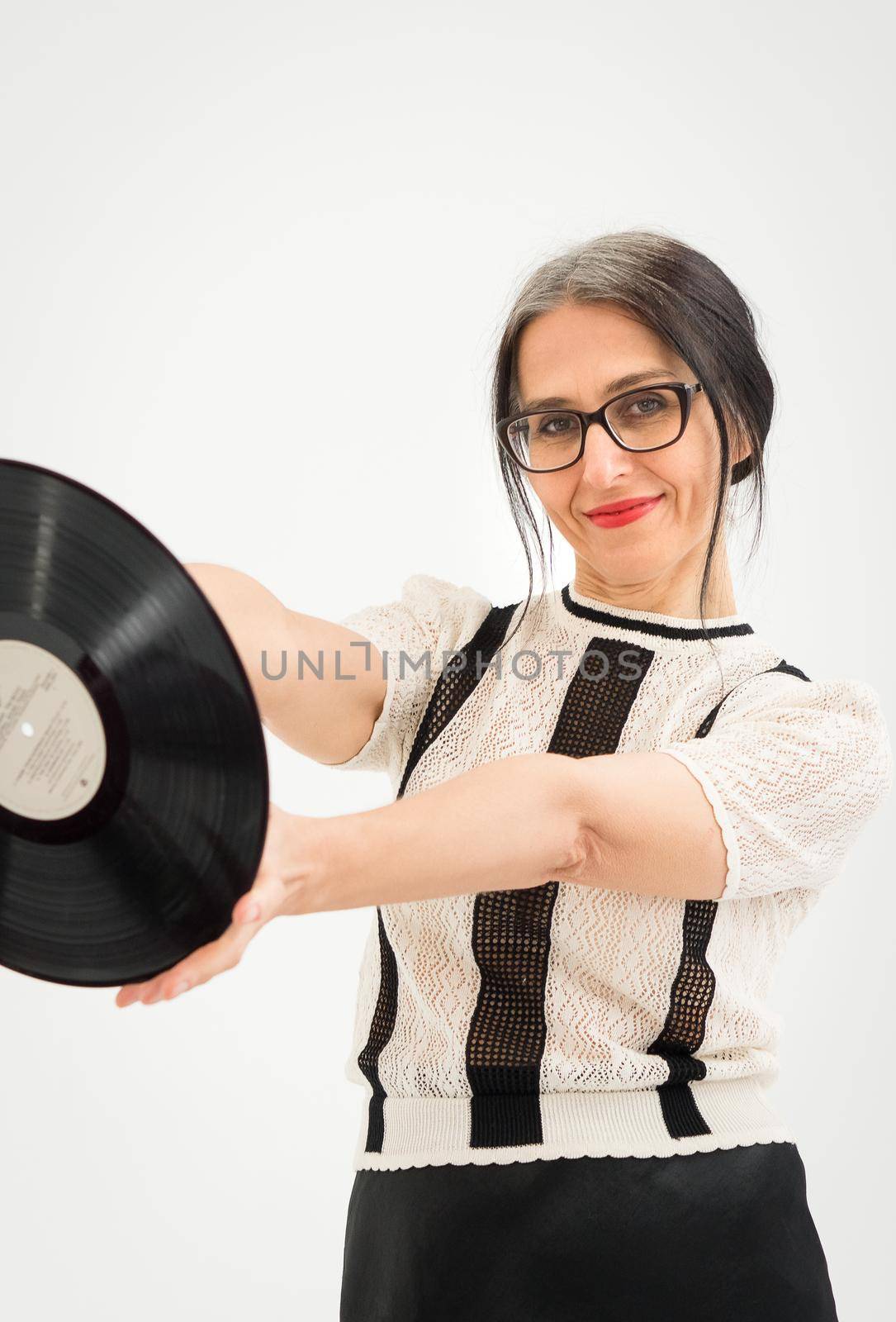 Studio photo of middle aged woman starting getting grey-haired wearing black and white clothes with vinyl record in hands on white background, middle age sexy lady, happy life concept.