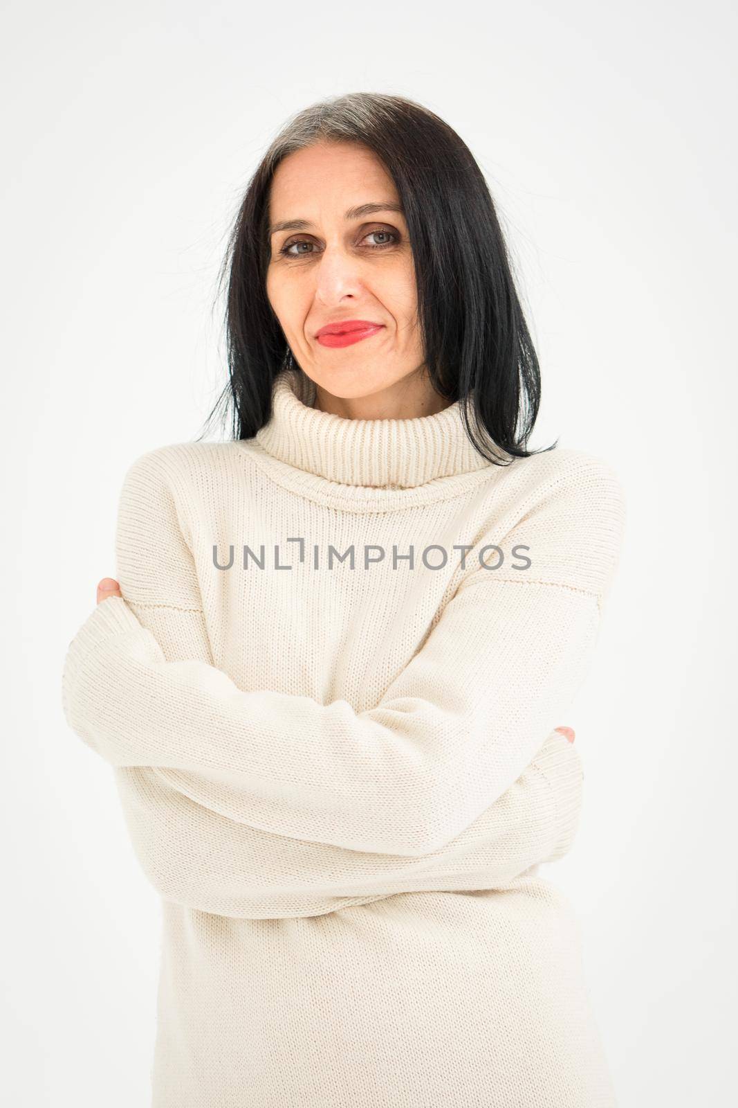 Middle aged woman starting getting grey-haired is posing in studio in sweater on white background, face skin care beauty, middle age skincare cosmetics, cosmetology concept.