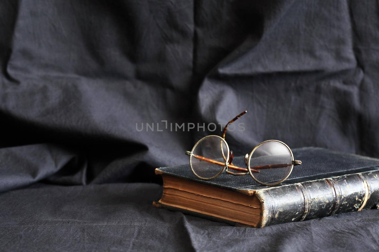 Old book and old glasses against dark textile beckground