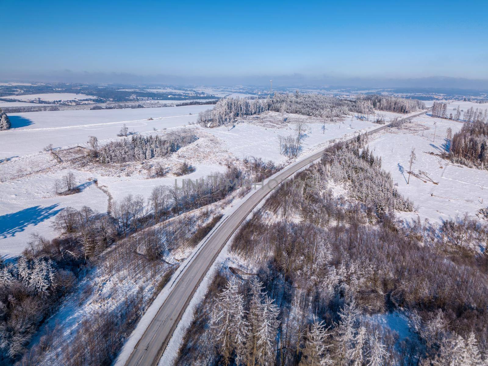 Aerial view of winter road, in sunny day. White frozen and snowy countryside landscape from bird eye, winter theme. Czech Republic, Vysocina region highland