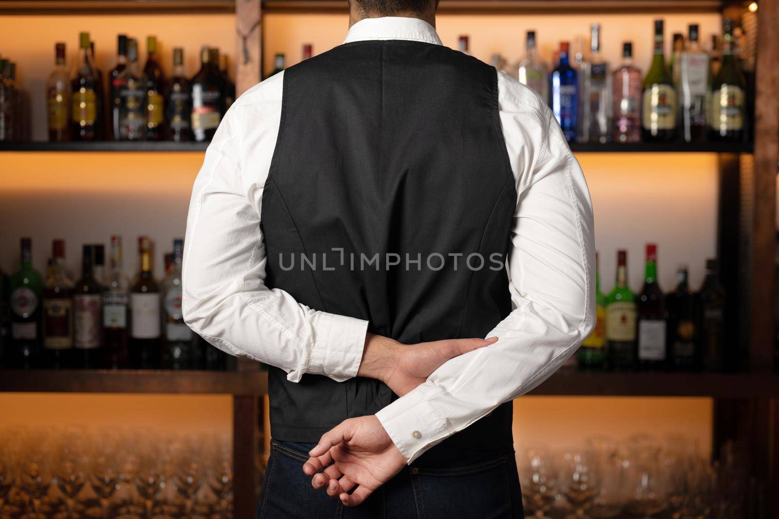 Backside of elegant bartender selecting beverage for customers in restaurant. by HERRAEZ