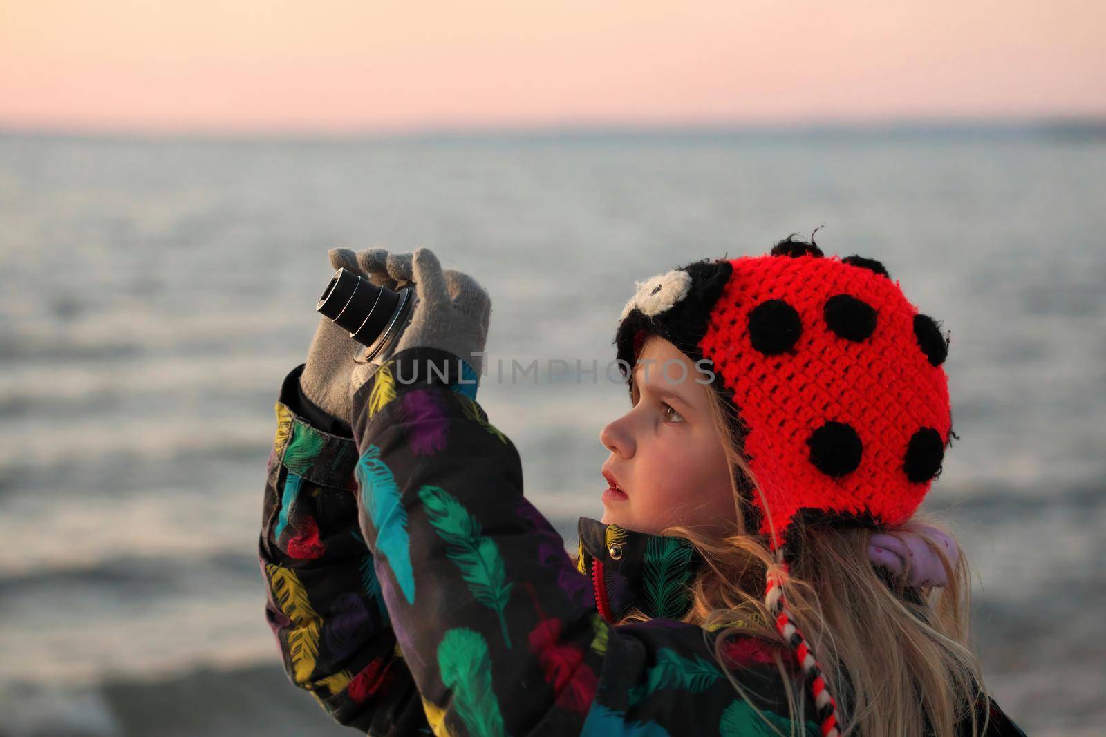 A 9 year old girls takes pictures with a camera at the beach at sunset. by markvandam